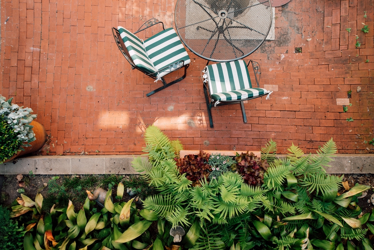 Charming brick patio with green-and-white striped chairs and lush garden plants, creating a relaxing outdoor oasis.