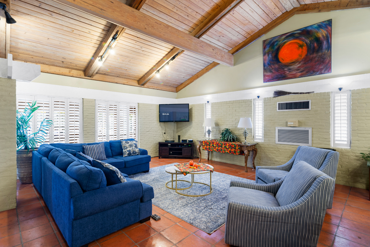 Inviting living room with a vaulted wooden ceiling, featuring a plush blue sectional sofa, elegant armchairs, and warm natural light.