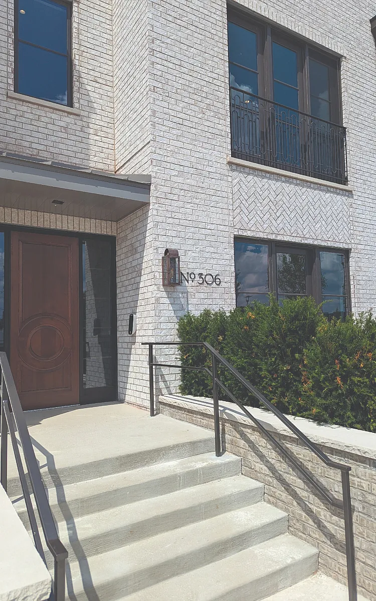 Chic modern entrance with white brick exterior and elegant dark wood door, featuring stylish metal stairs and lush greenery beside number 306.