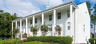 Elegant colonial-style apartment building with white pillars, lush greenery, and bright blue skies, offering a serene and picturesque living environment.