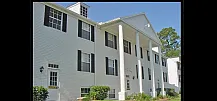Charming colonial-style apartment building with white brick exterior and iconic columns, surrounded by lush greenery.