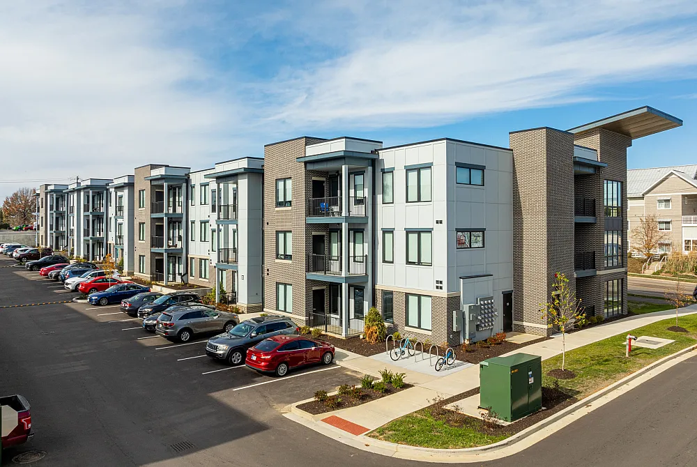 Modern apartment complex with sleek architecture, spacious balconies, and ample parking under a clear blue sky.