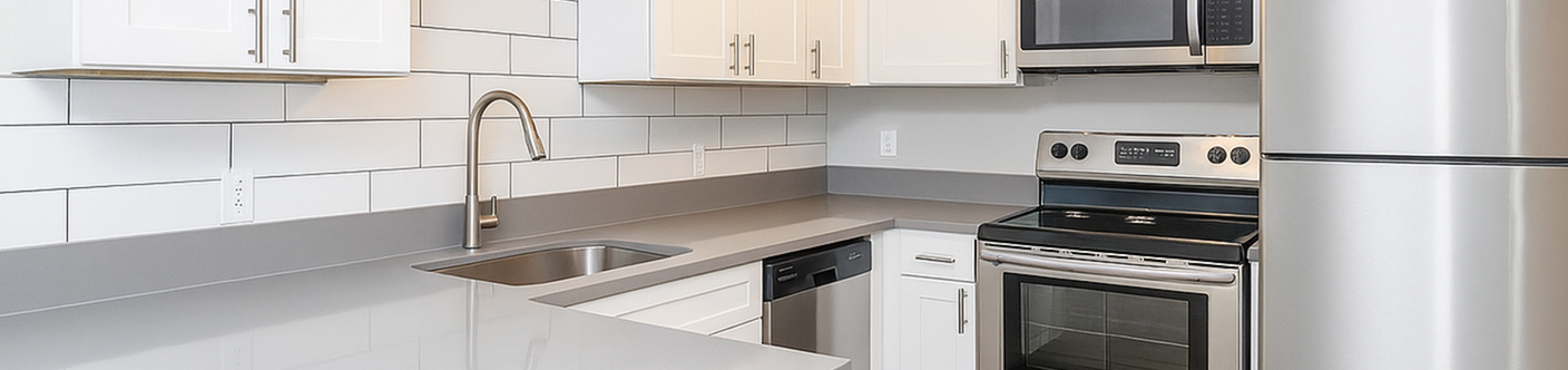 Modern kitchen with sleek stainless steel appliances, pristine white cabinetry, and elegant gray countertops.