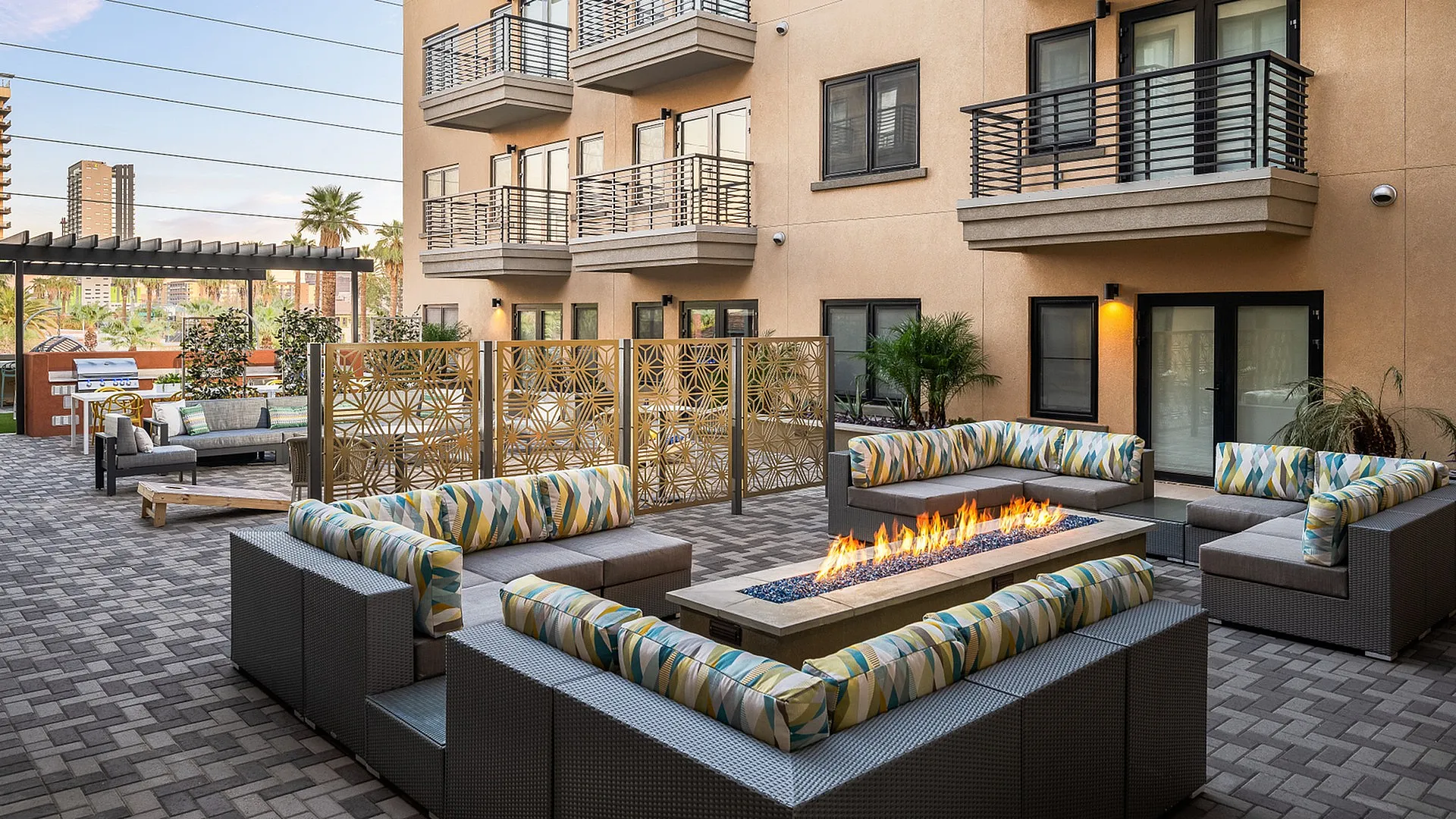 Elegant outdoor apartment courtyard featuring stylish seating around a modern fire pit, framed by intricate metal screens and lush greenery.