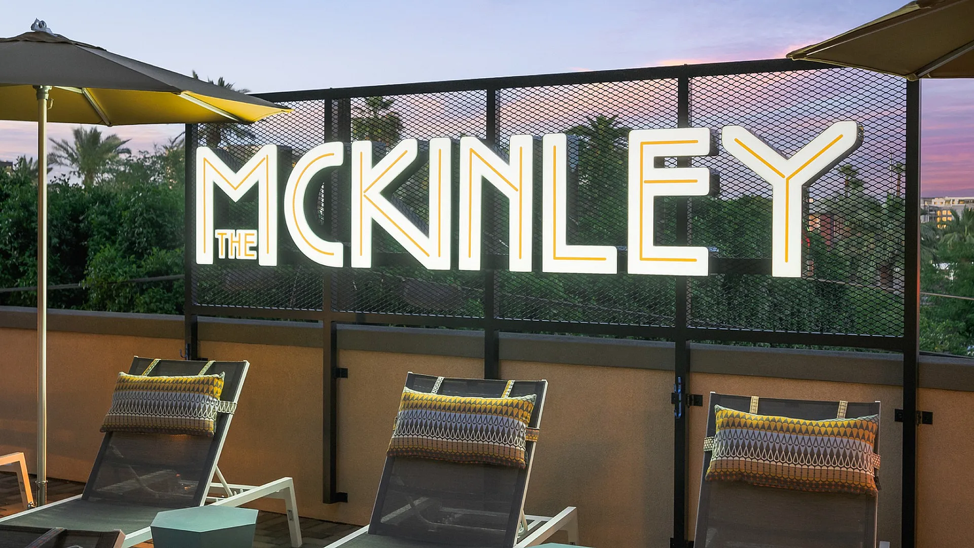 Inviting outdoor lounge area at The McKinley with elegant lighting, plush sun loungers, and a serene sunset backdrop.