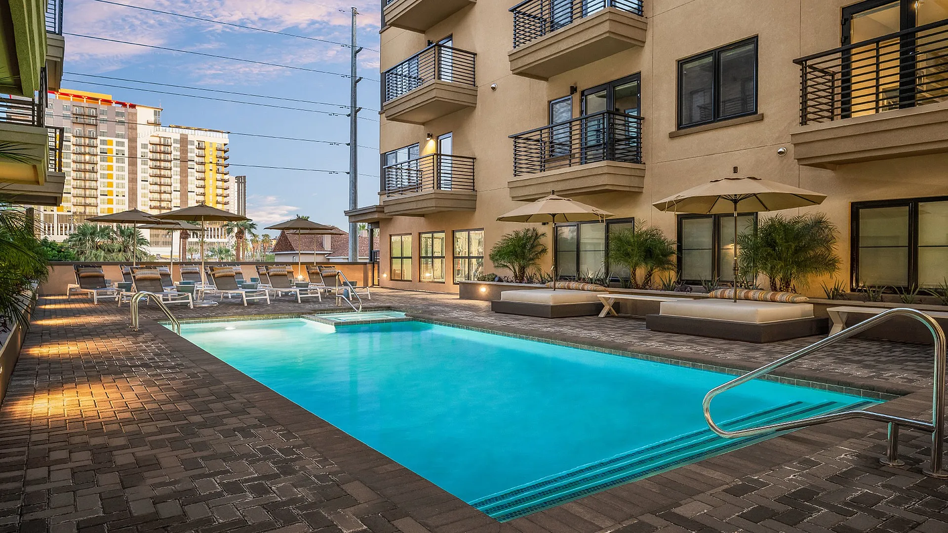 Stunning apartment complex featuring a sparkling outdoor pool with stylish lounge chairs and green plants, perfect for relaxation and luxury living.