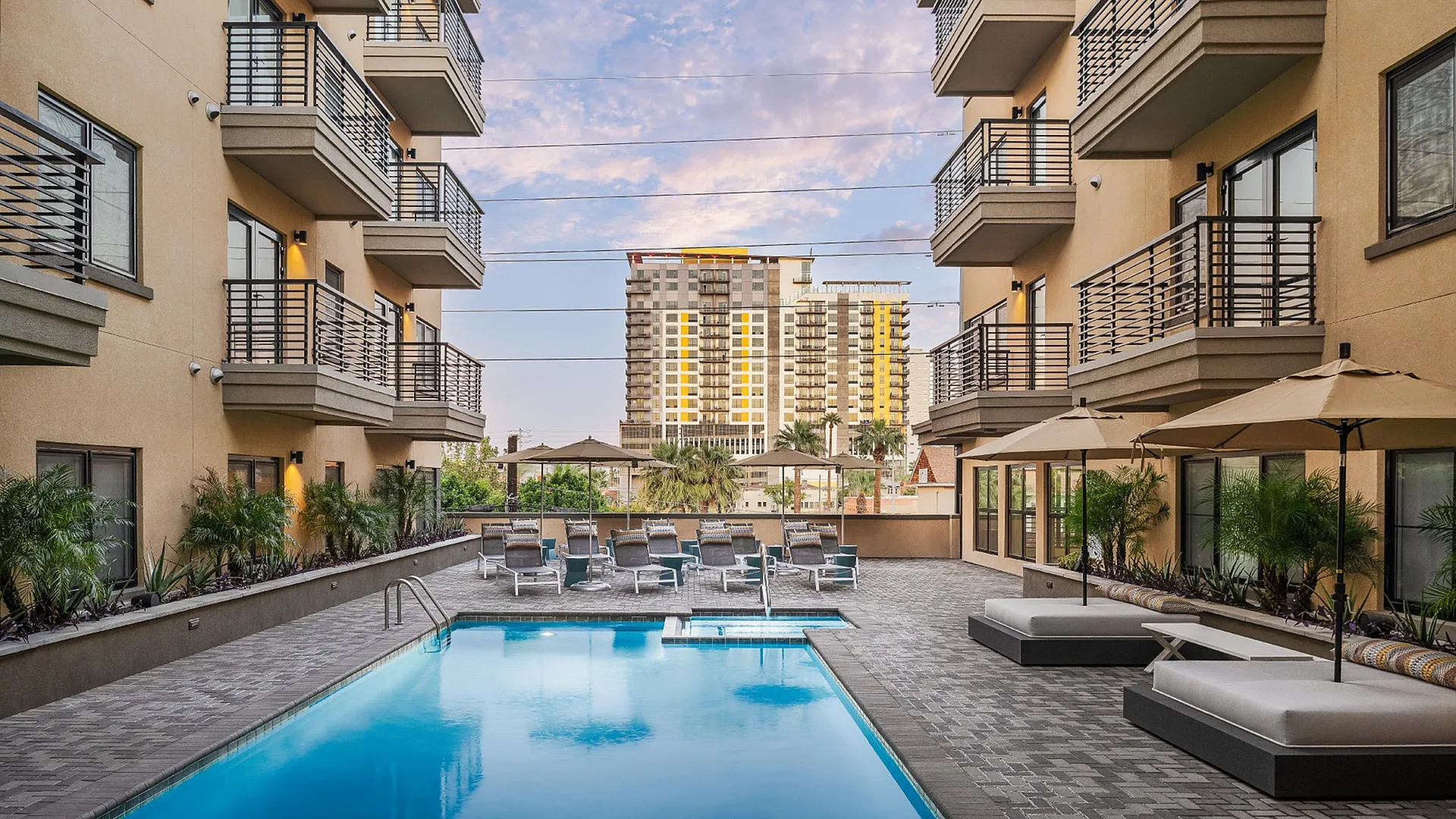 Luxe urban apartment complex featuring a pristine outdoor pool, chic lounge chairs, and elegant balconies against a vibrant city backdrop.