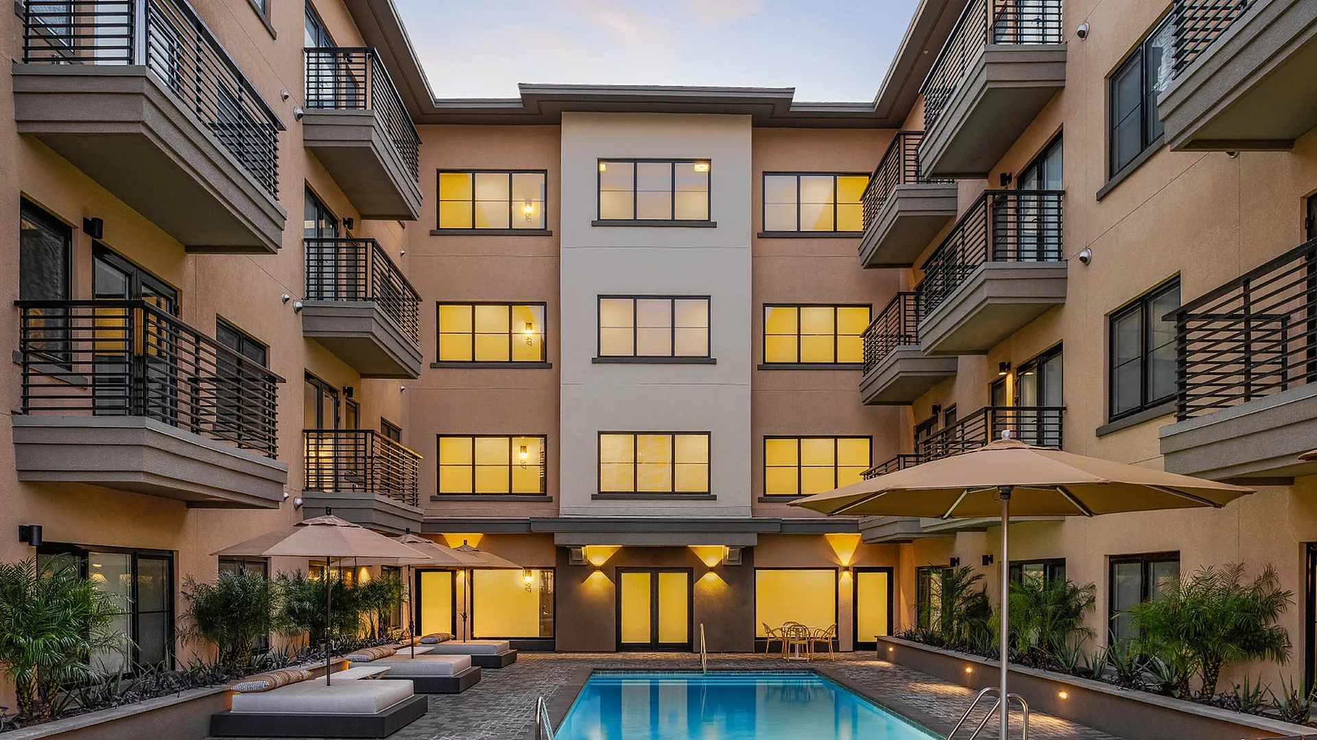 Luxurious apartment complex courtyard featuring a serene swimming pool, stylish balcony views, and ambient evening lighting.
