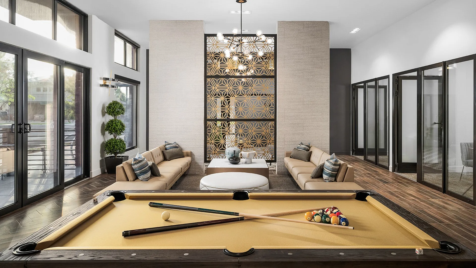 Sophisticated apartment lounge featuring a modern pool table, elegant seating, and stylish decor with natural light streaming through large windows.