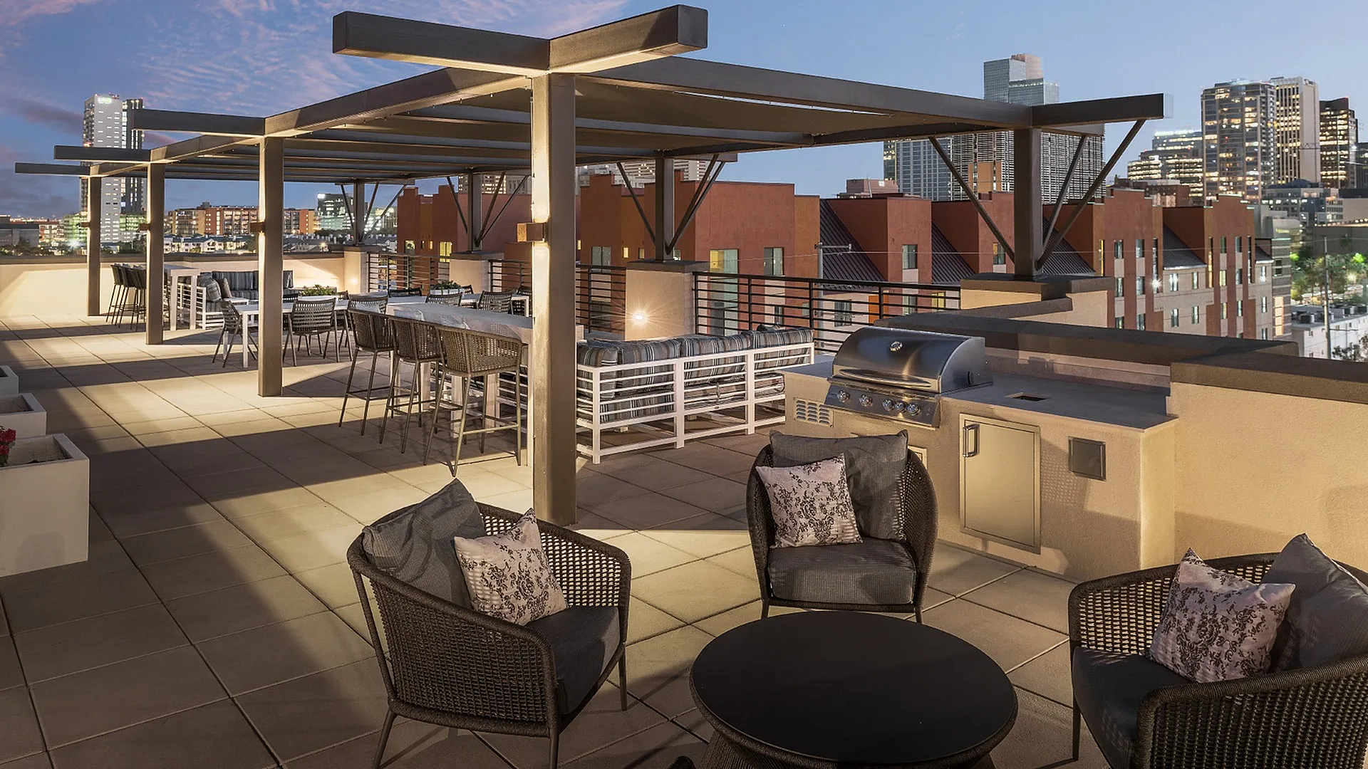 Chic rooftop patio with modern seating and grill, offering stunning city skyline views at dusk.