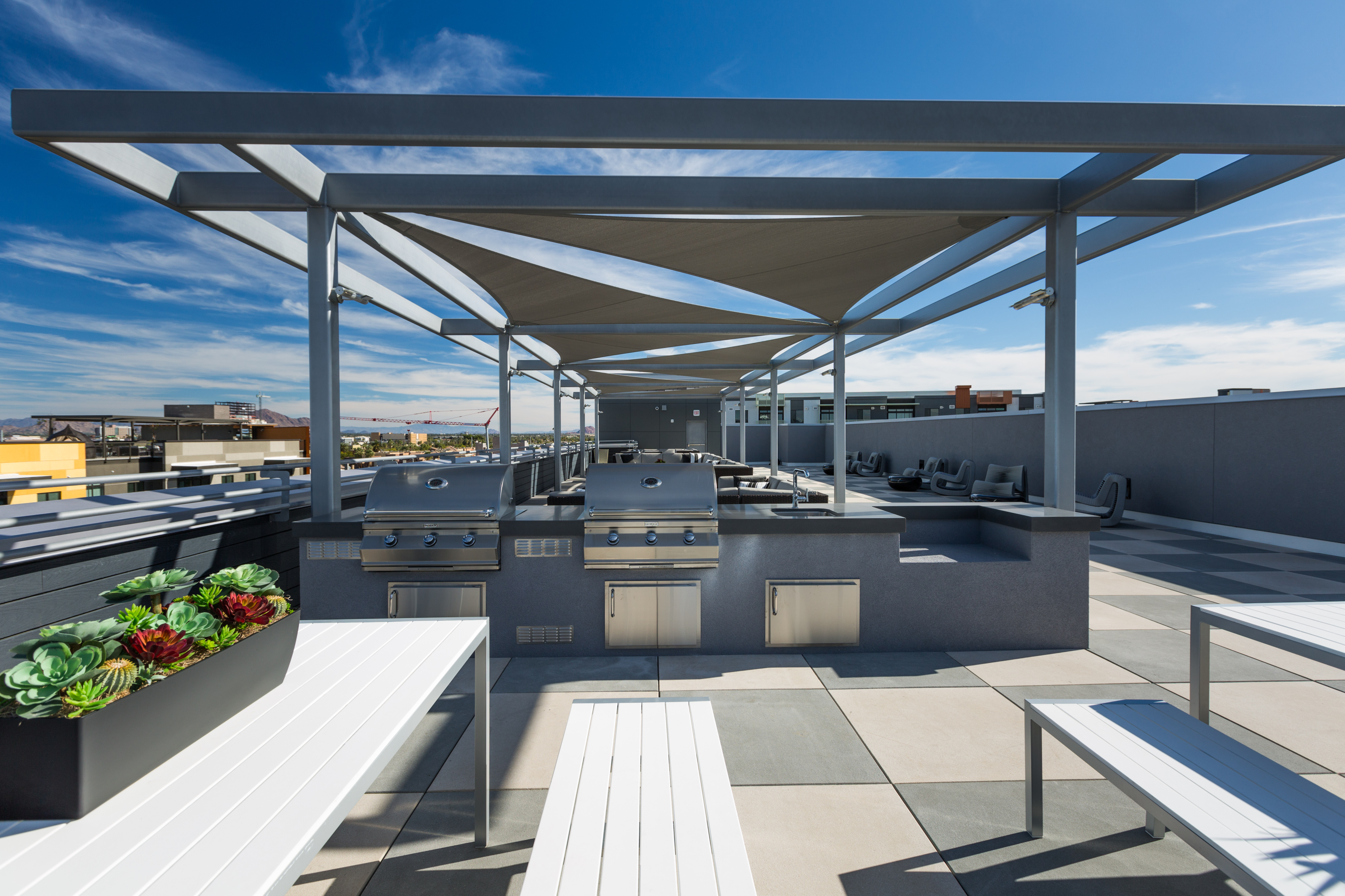 Modern rooftop terrace with sleek outdoor kitchen, stainless steel grills, and stylish seating under a clear blue sky.