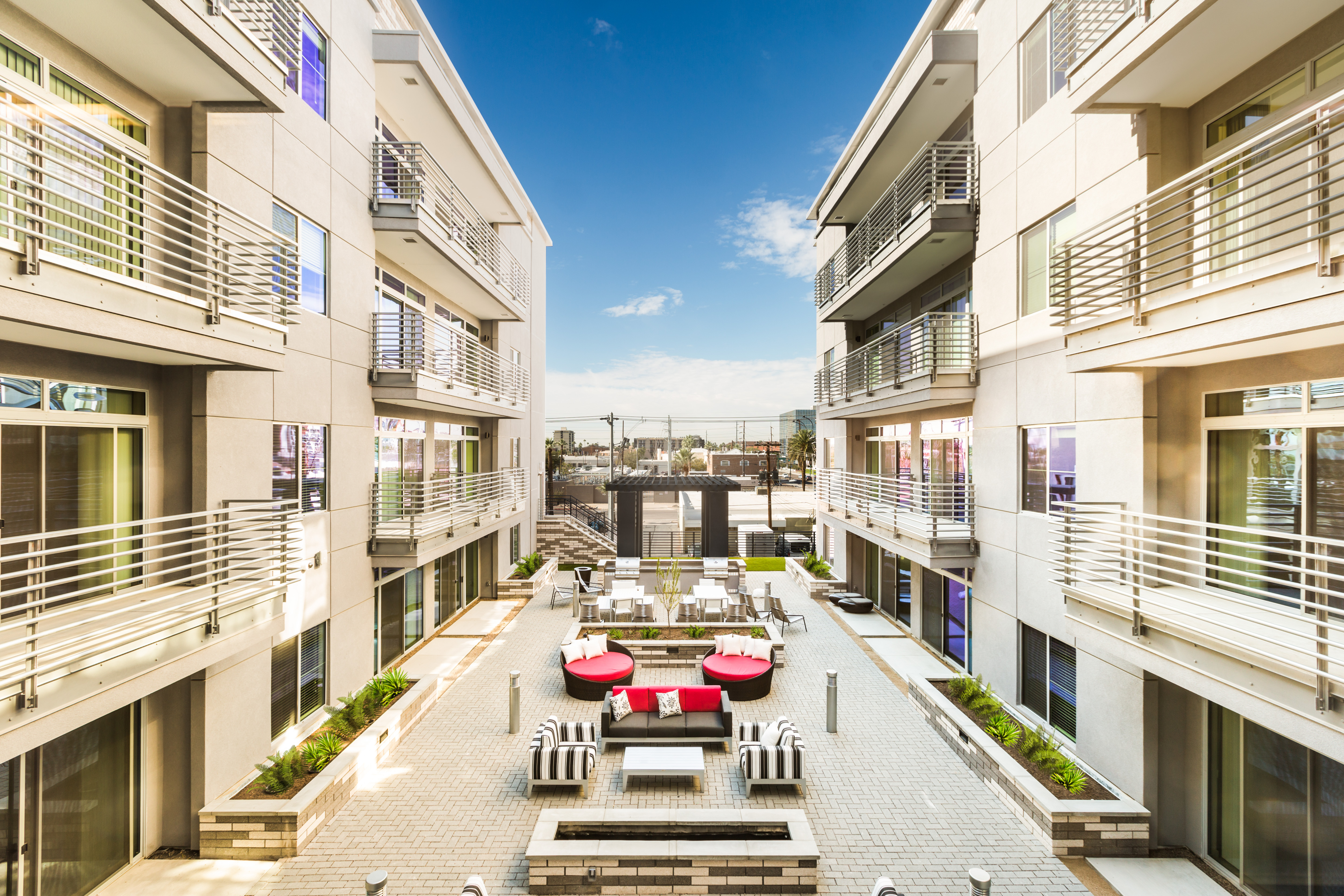 Modern apartment complex showcasing elegant balconies and a stylish courtyard with chic outdoor seating, set against a bright blue sky.