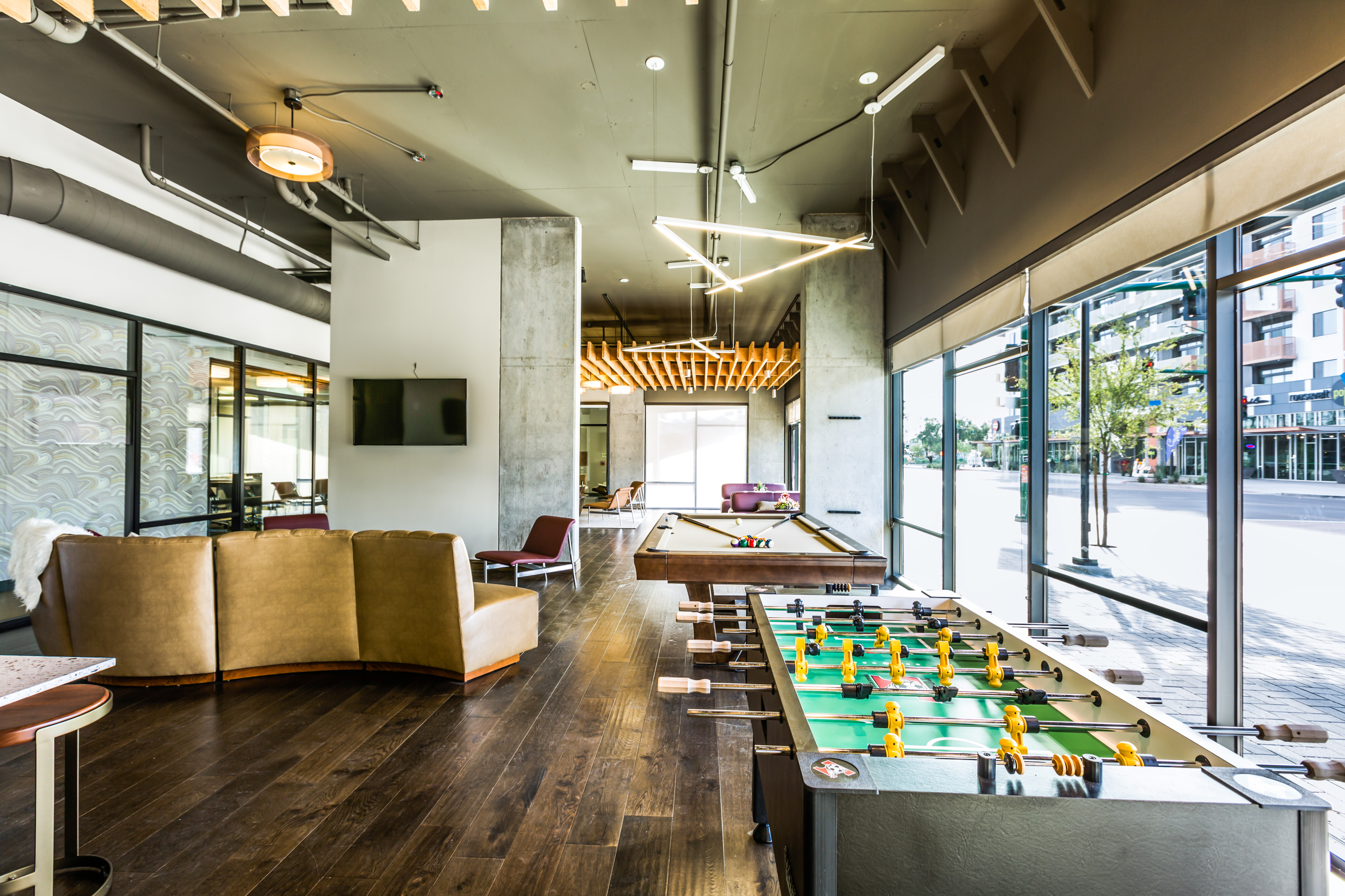 Modern communal space featuring sleek leather couches, stylish pool and foosball tables, with expansive windows offering vibrant city views.
