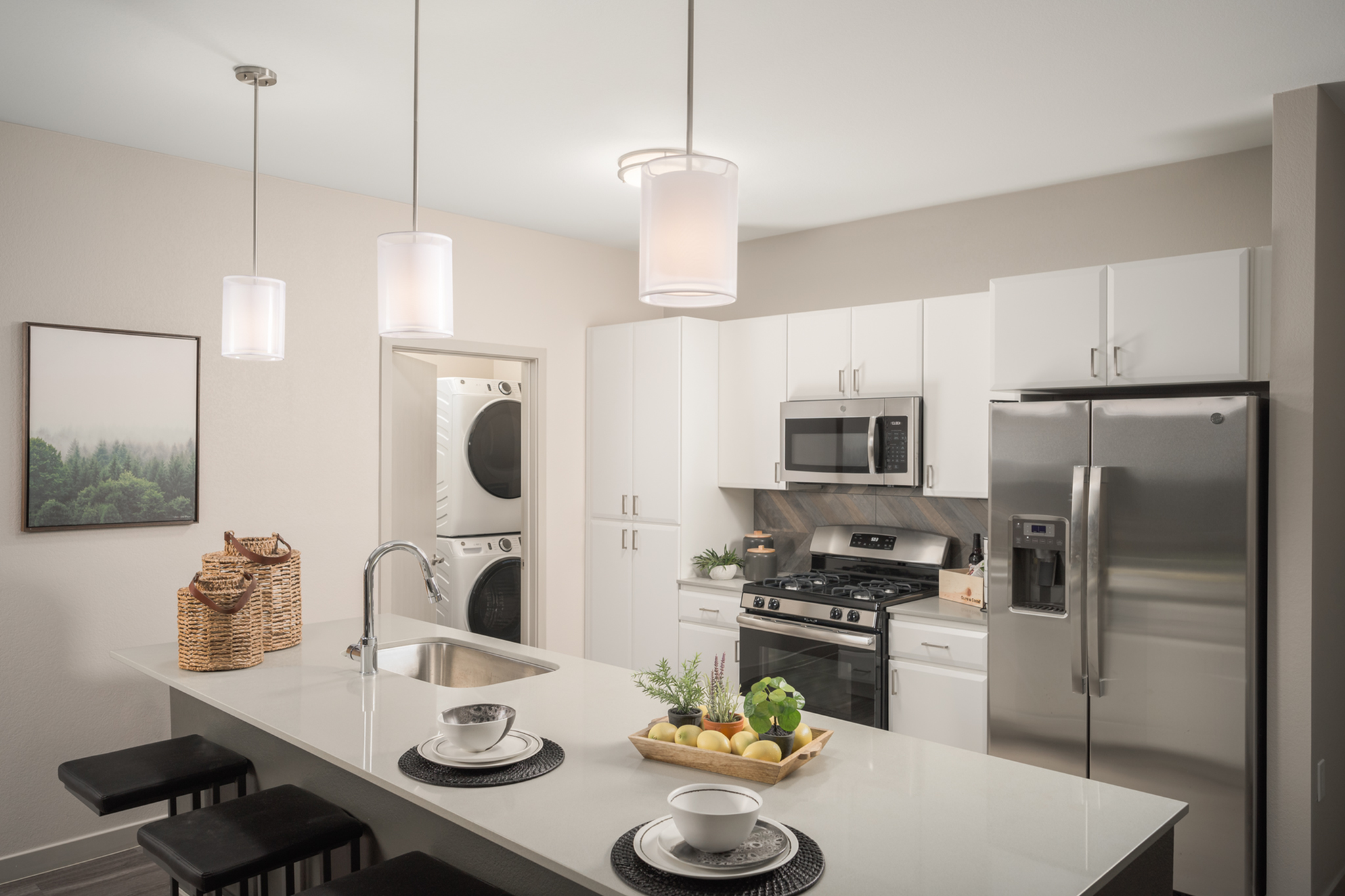Modern kitchen with sleek stainless steel appliances, elegant pendant lighting, and a stylish breakfast bar. Bright and inviting space featuring integrated laundry facilities.