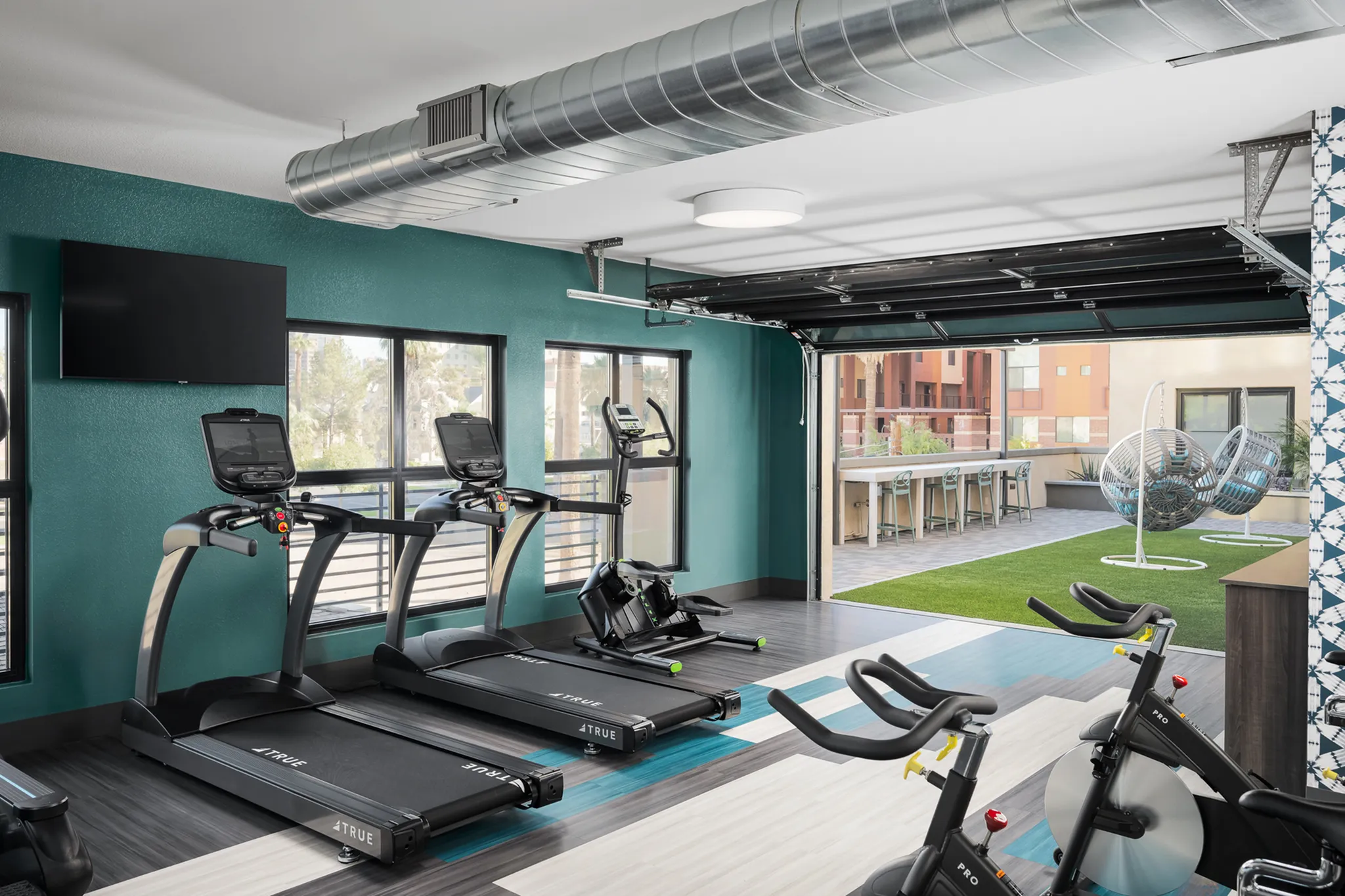 Modern fitness center featuring state-of-the-art treadmills, exercise bikes, and a vibrant outdoor seating area with lush greenery.