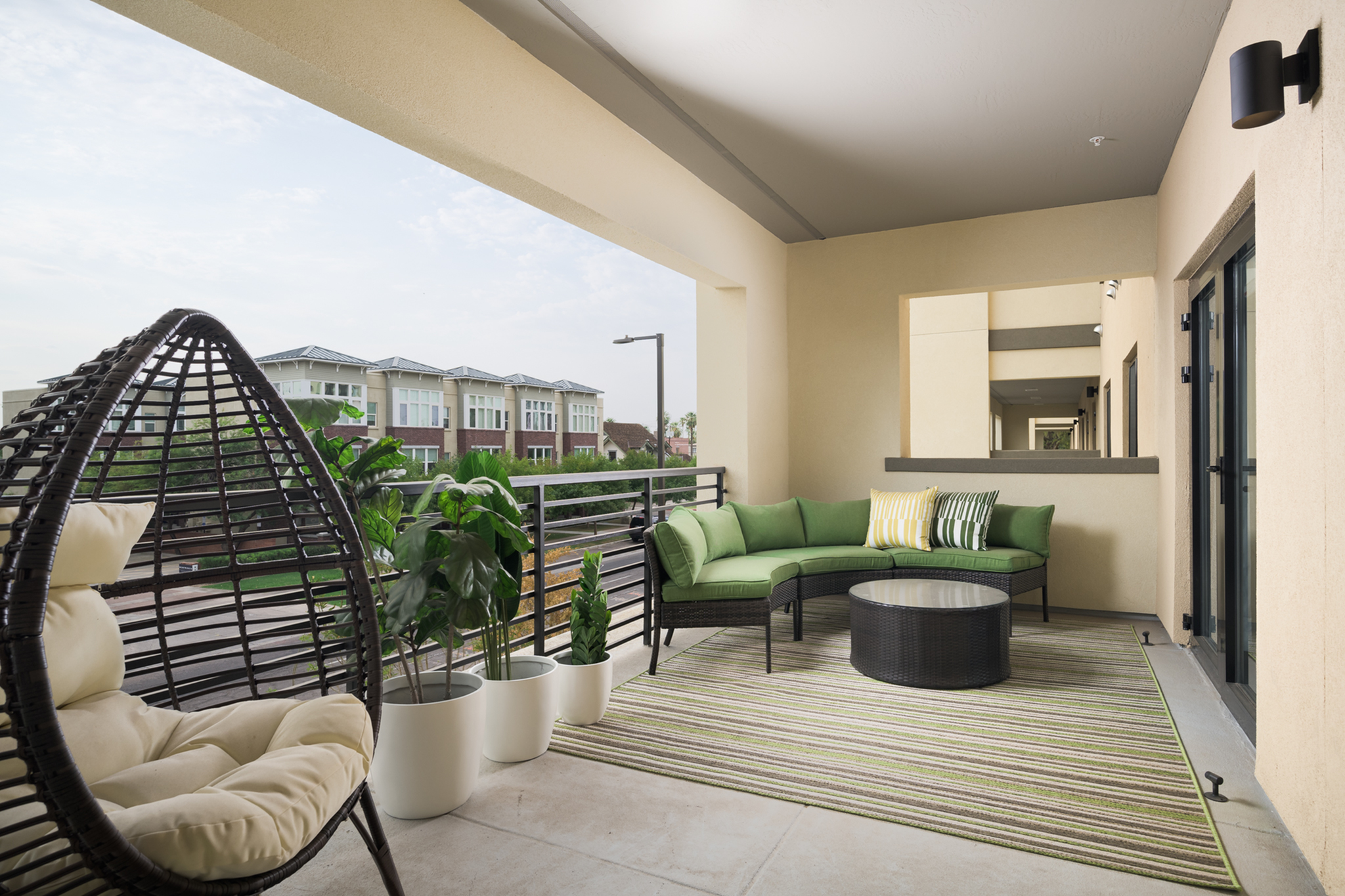 Inviting balcony with modern wicker lounge chair, vibrant green sectional sofa, potted plants, and scenic views.