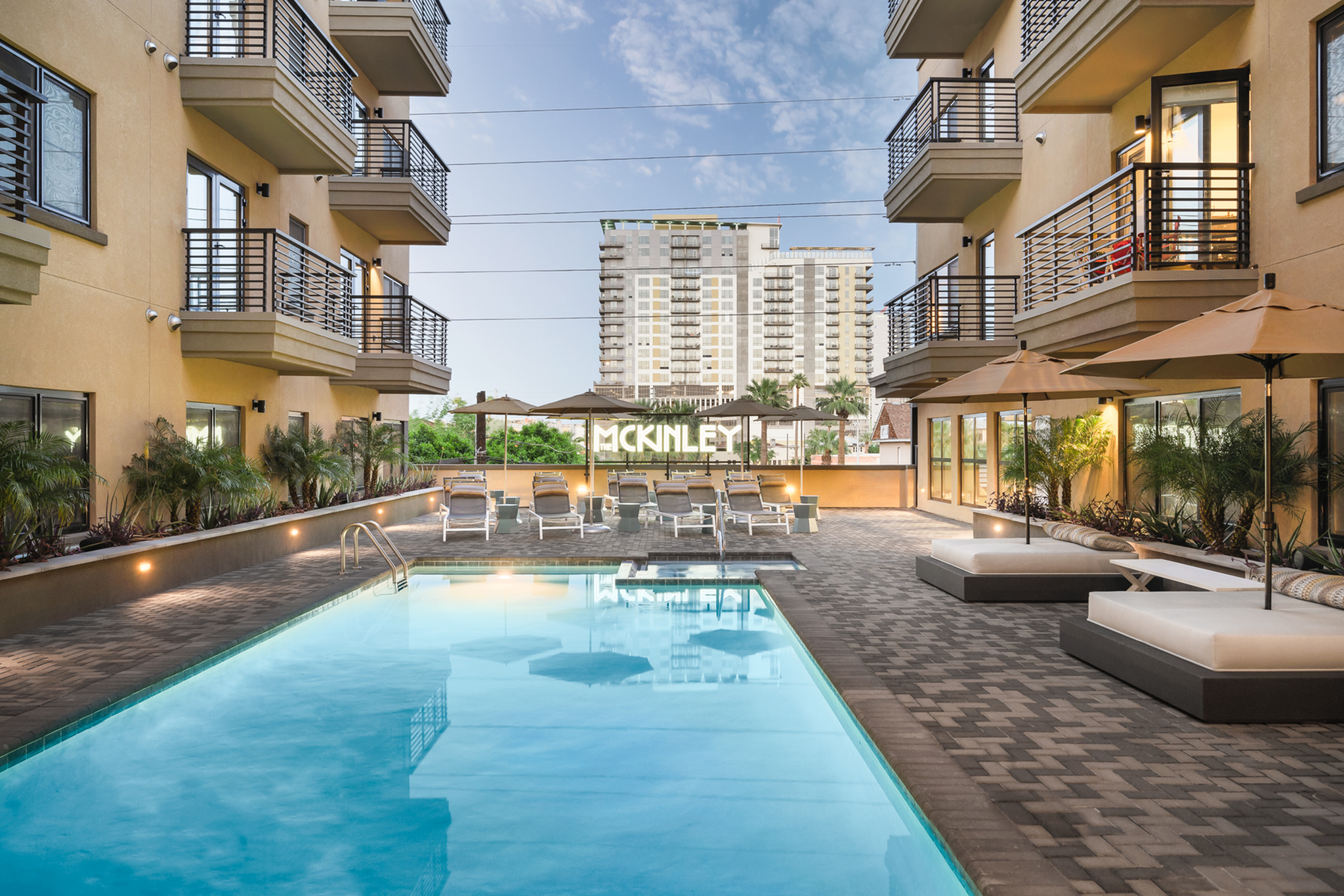 Modern apartment complex featuring a stunning swimming pool, lounge seating, and private balconies, ideal for luxury living.