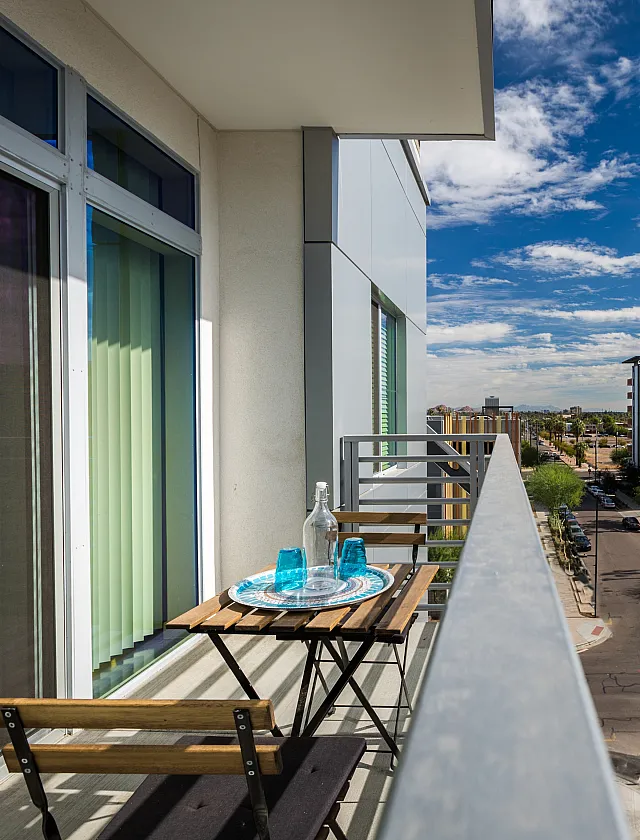 Modern apartment balcony with a charming city view, featuring a cozy outdoor dining setup under a brilliant blue sky.