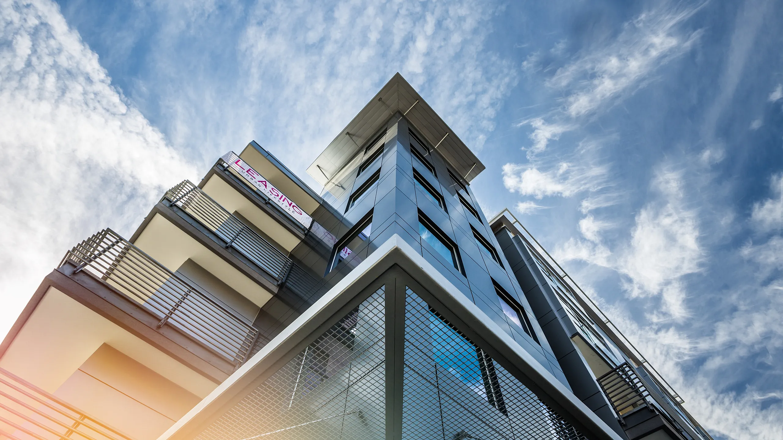 Modern urban apartment building with sleek design and spacious balconies against a vibrant blue sky.