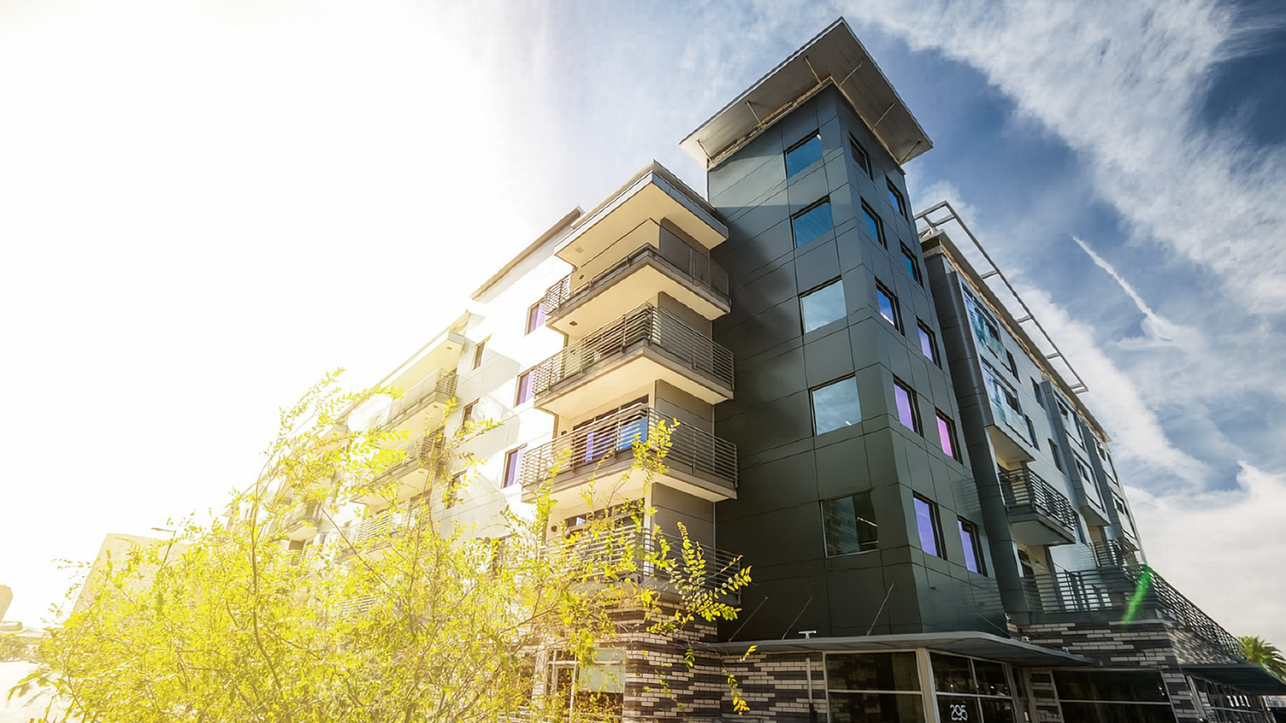 Modern residential building with stylish balconies and sleek design, set against a vibrant blue sky, bathed in sunlight.