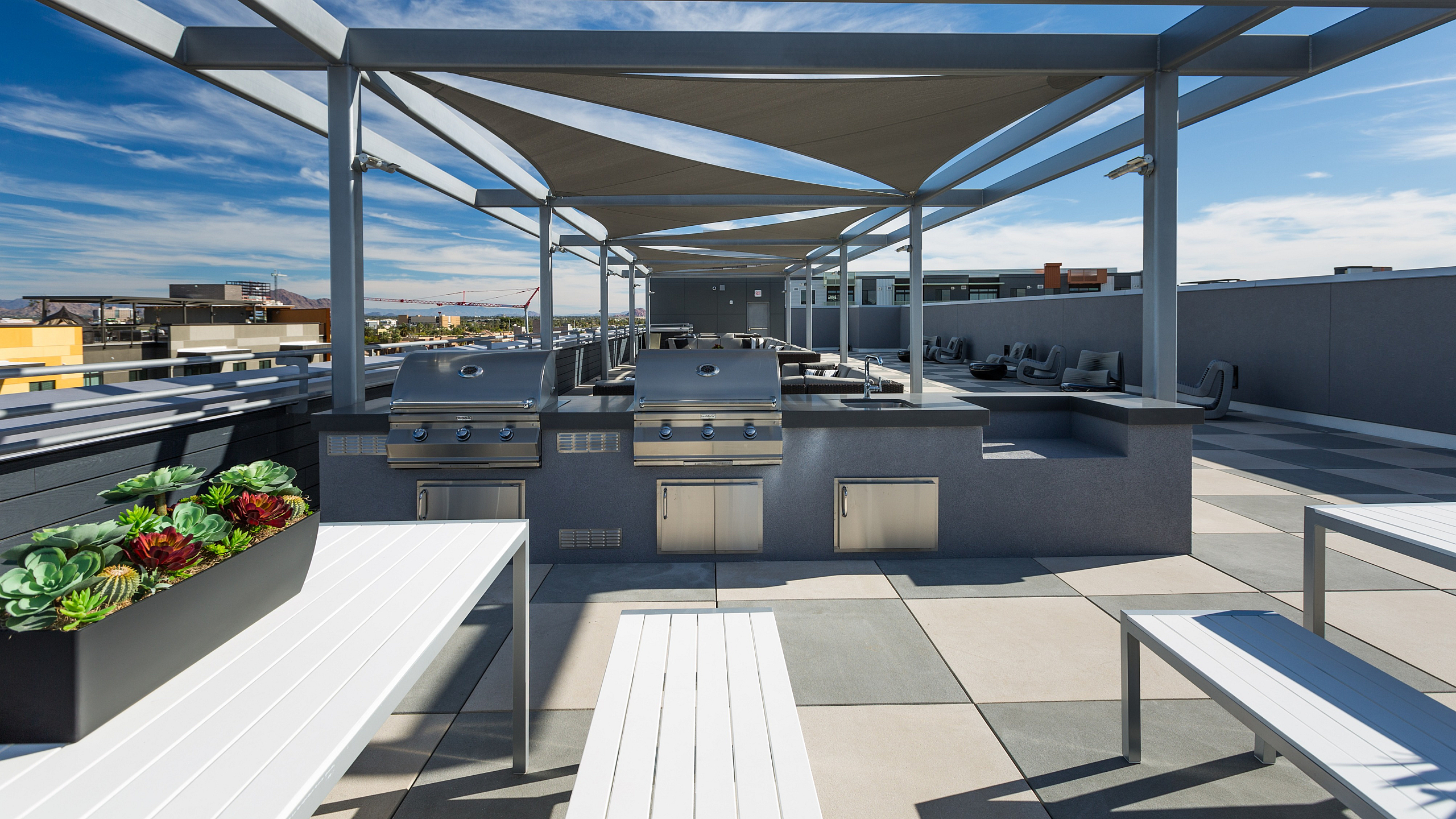 Modern rooftop terrace with shaded seating, sleek outdoor grills, and scenic city views.