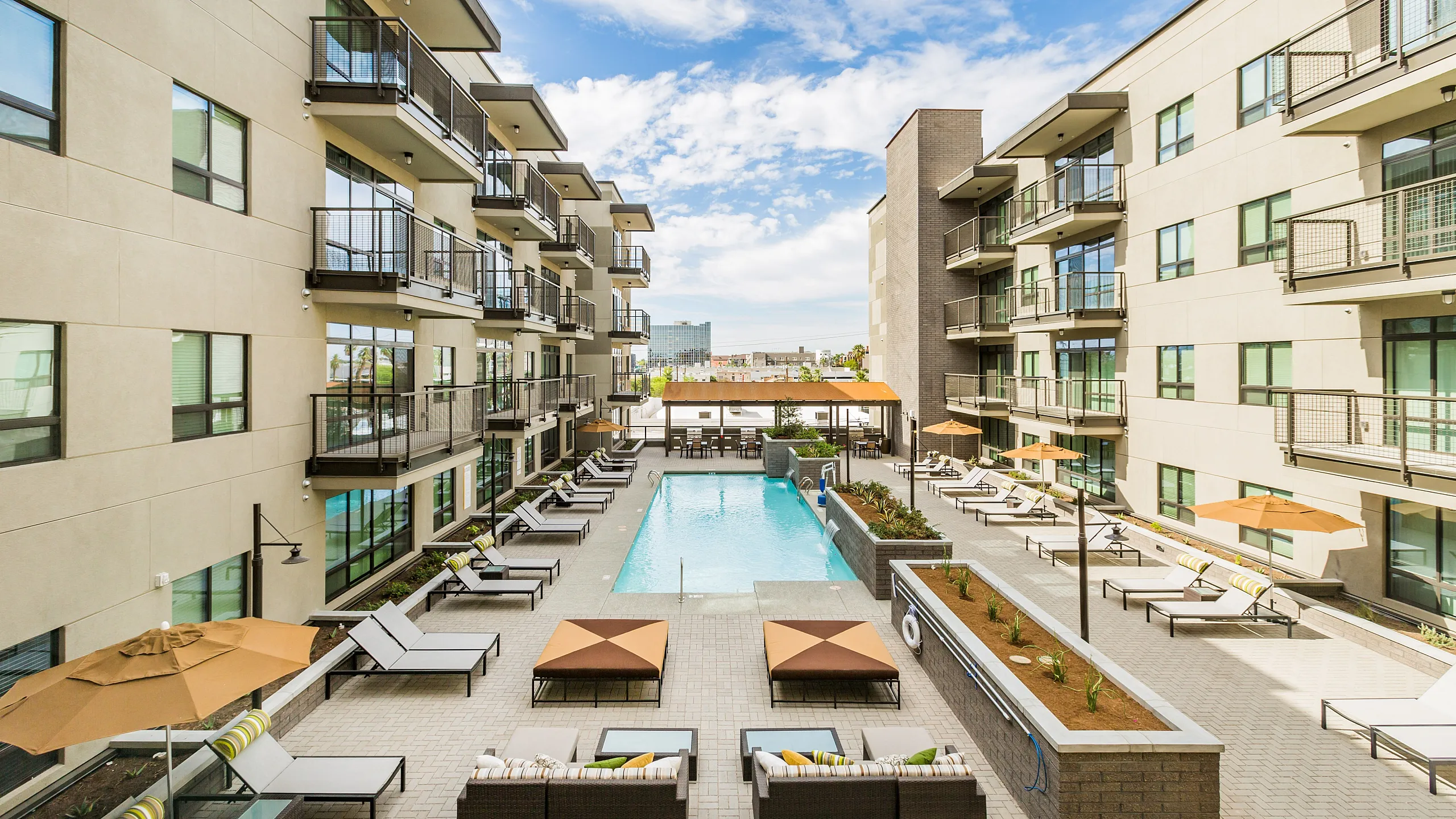 Modern apartment complex with a luxurious outdoor swimming pool, surrounded by stylish loungers and shaded seating areas, offering a relaxing community atmosphere.
