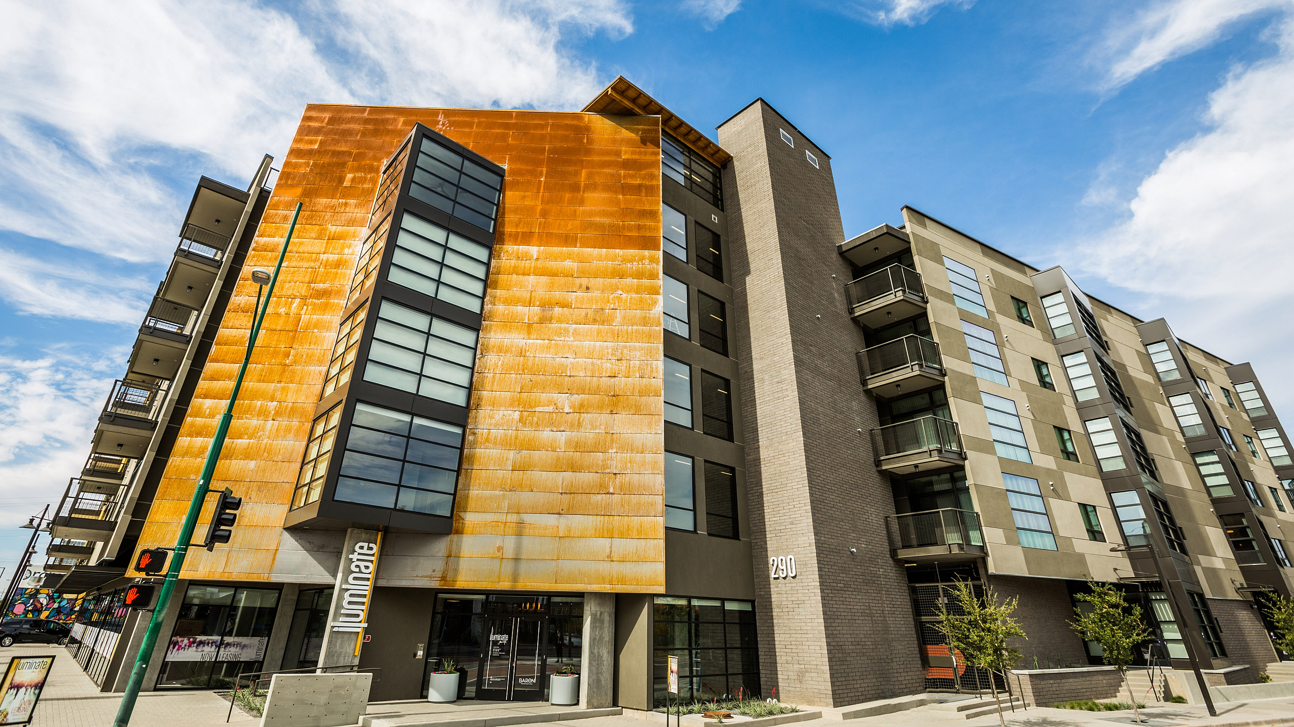 Modern urban apartment building with a striking rust-colored facade and sleek glass windows under a vibrant blue sky.