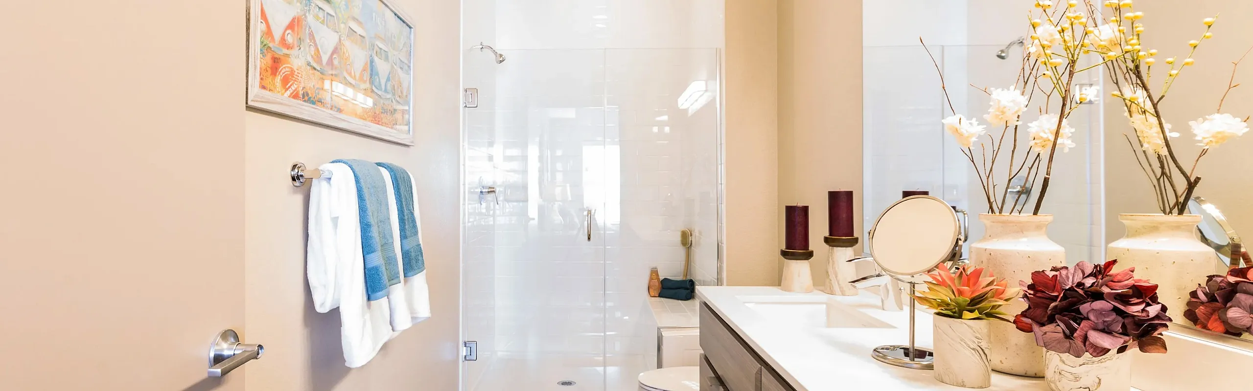 Elegant bathroom with modern fixtures, large vanity mirror, and stylish decor. Features glass shower, plush towels, and vibrant floral accents for a refreshing and welcoming ambiance.