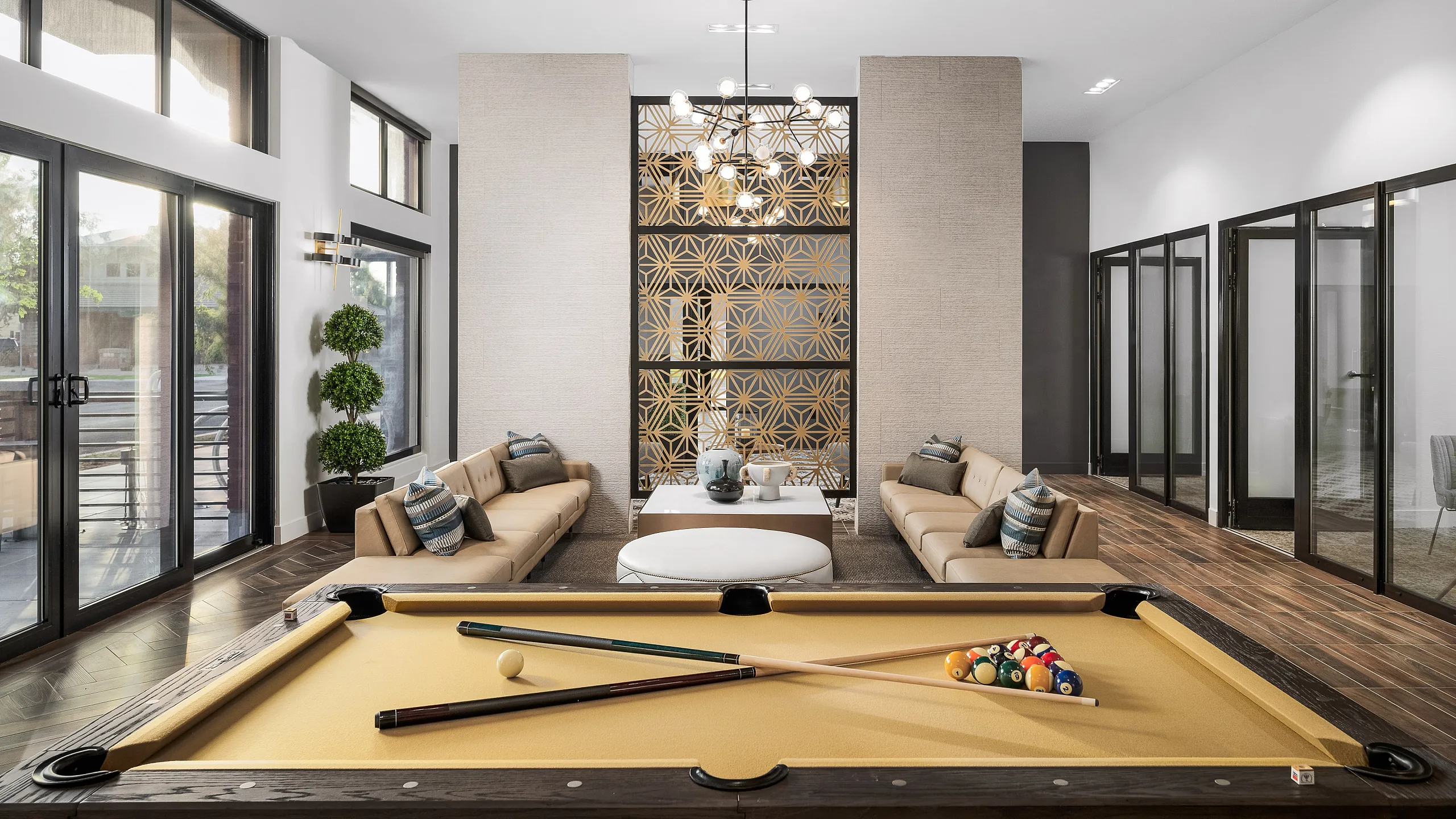 Luxurious modern lounge featuring a sleek pool table, elegant decor, and ample natural light through large windows.