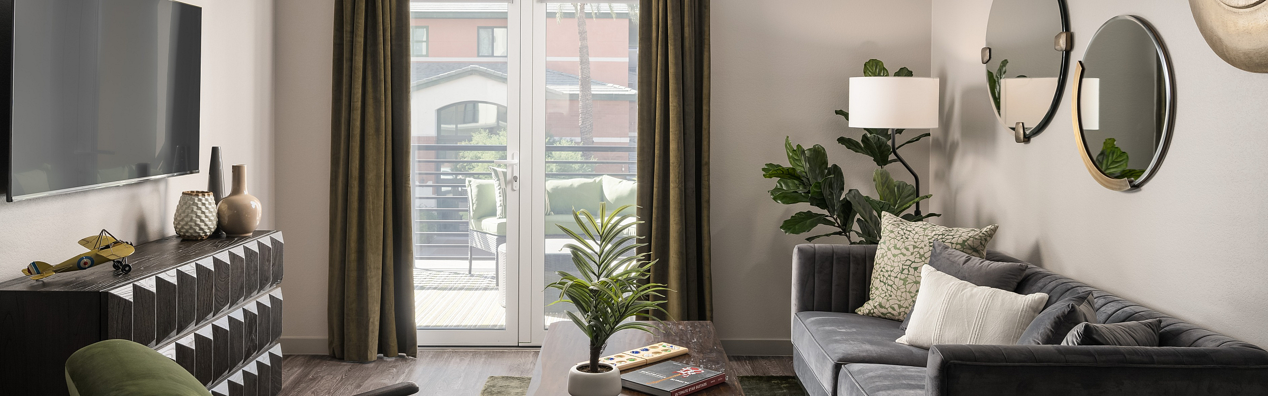 Modern living room with a cozy gray sofa, sleek wooden furniture, and vibrant green accents, featuring a stylish ceiling fan and sliding doors opening to a sunny balcony.