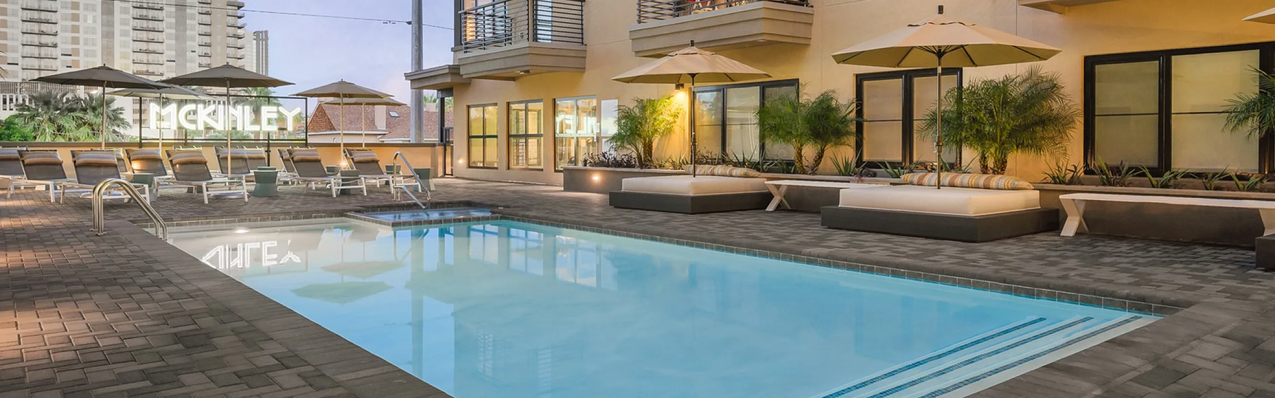 Modern apartment complex with a luxurious pool area surrounded by stylish loungers and elegant balconies, offering a sophisticated urban living atmosphere.
