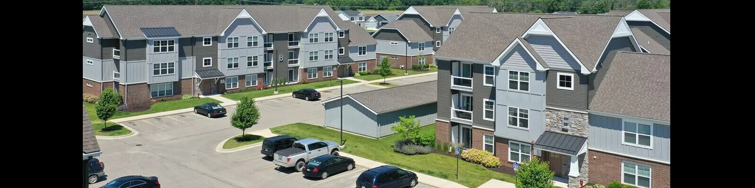 Charming aerial view of modern apartment complex with landscaped greenery and ample parking.