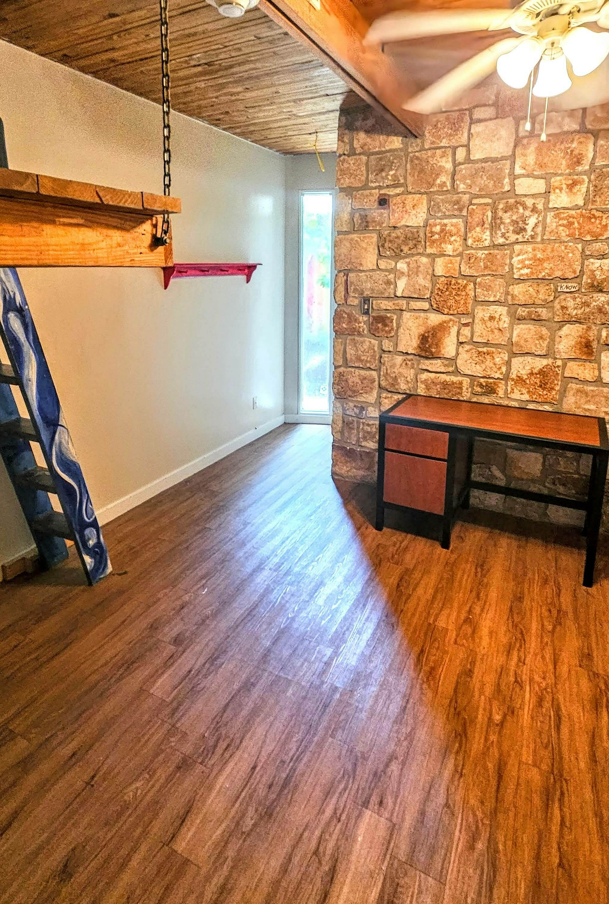 Charming room with rustic stone accent wall, stylish wooden ceiling, and sleek laminate flooring, offering a cozy and inviting atmosphere.