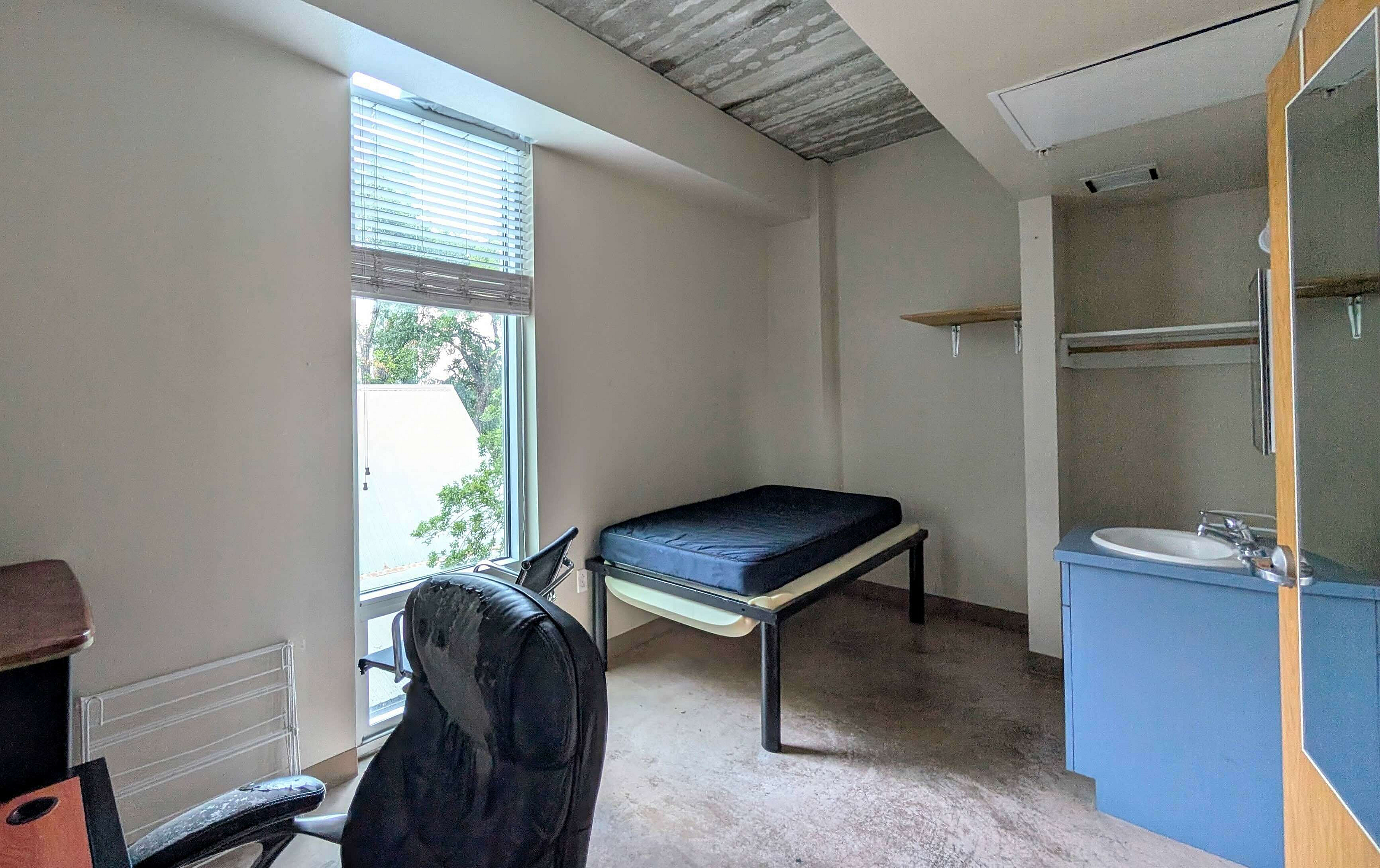 Cozy bedroom featuring a large window, a sleek desk chair, and a minimalist bed with adjacent vanity.