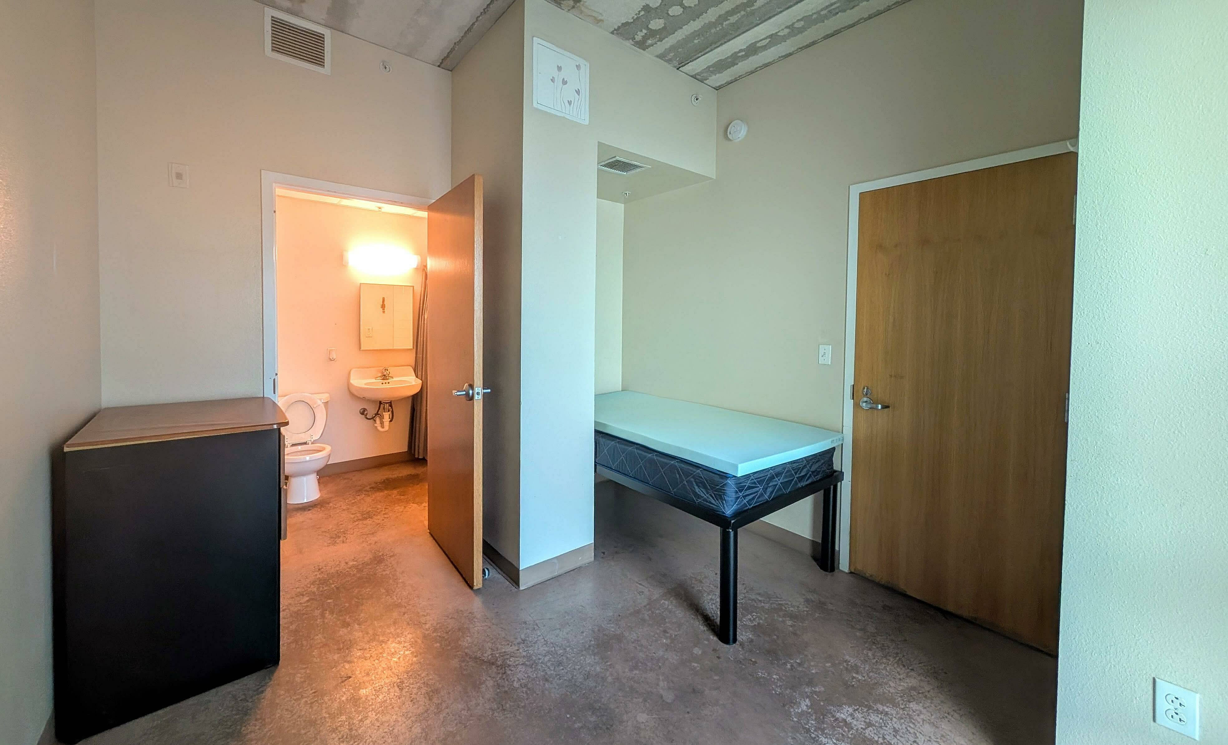 Bright bedroom with cozy bed, minimalist furniture, and en-suite bathroom in a modern apartment.