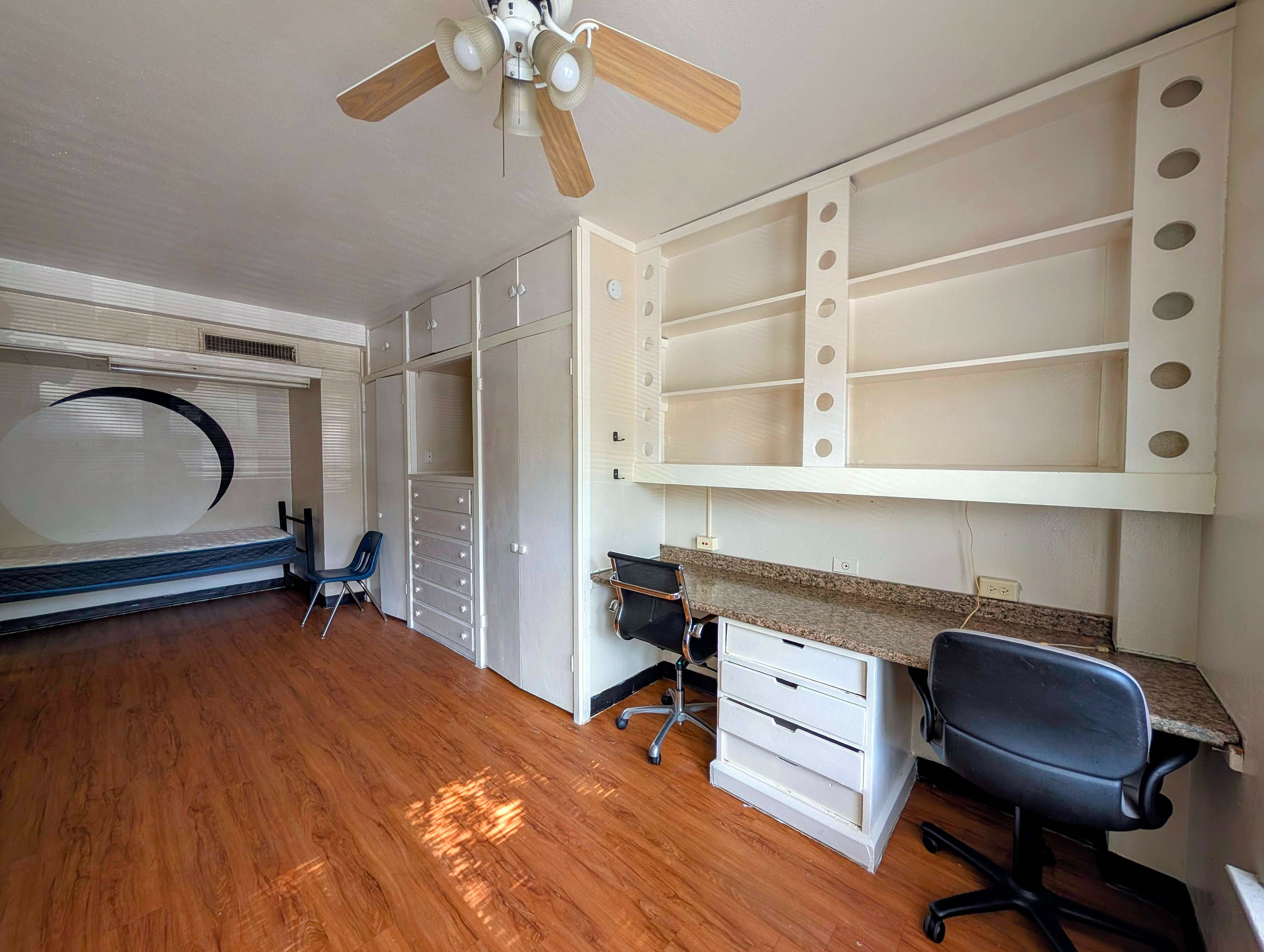 Spacious room with elegant wood flooring, stylish built-in desks, ample storage, and a unique wall design enhancing modern living.