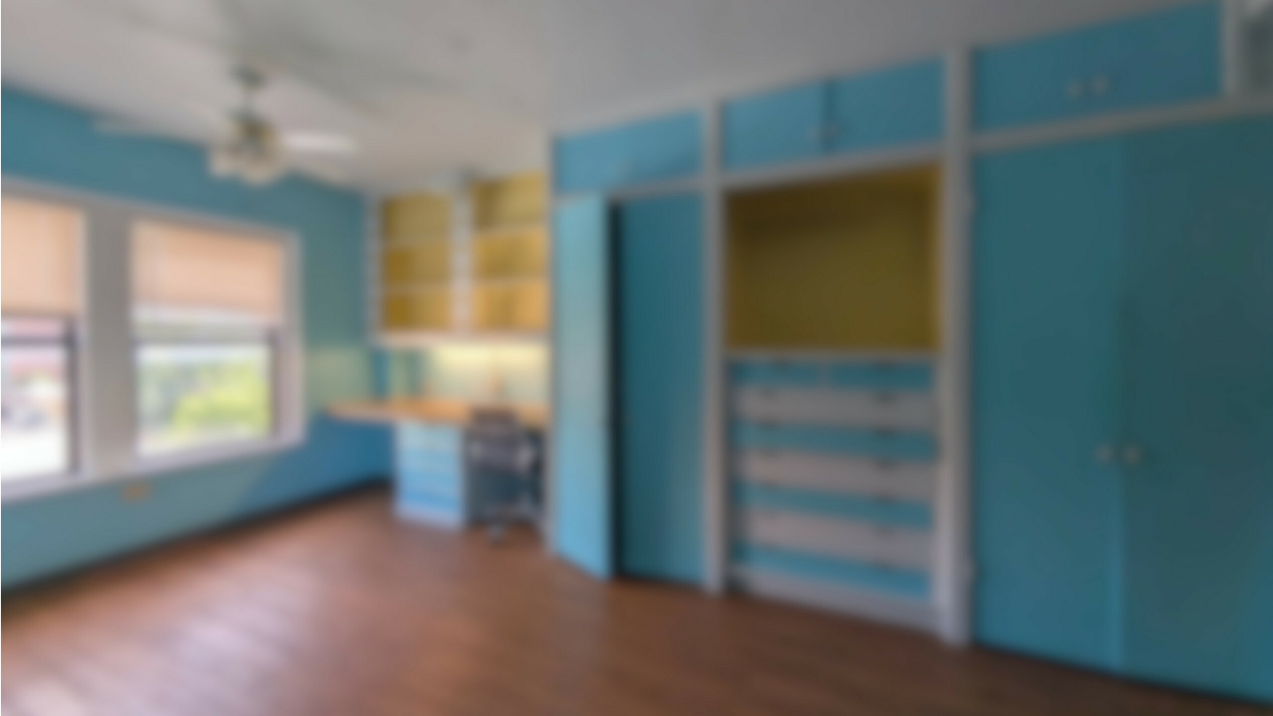Bright and airy room with large windows, vibrant blue built-in storage, and warm wooden floors, perfect for a creative workspace or cozy retreat.