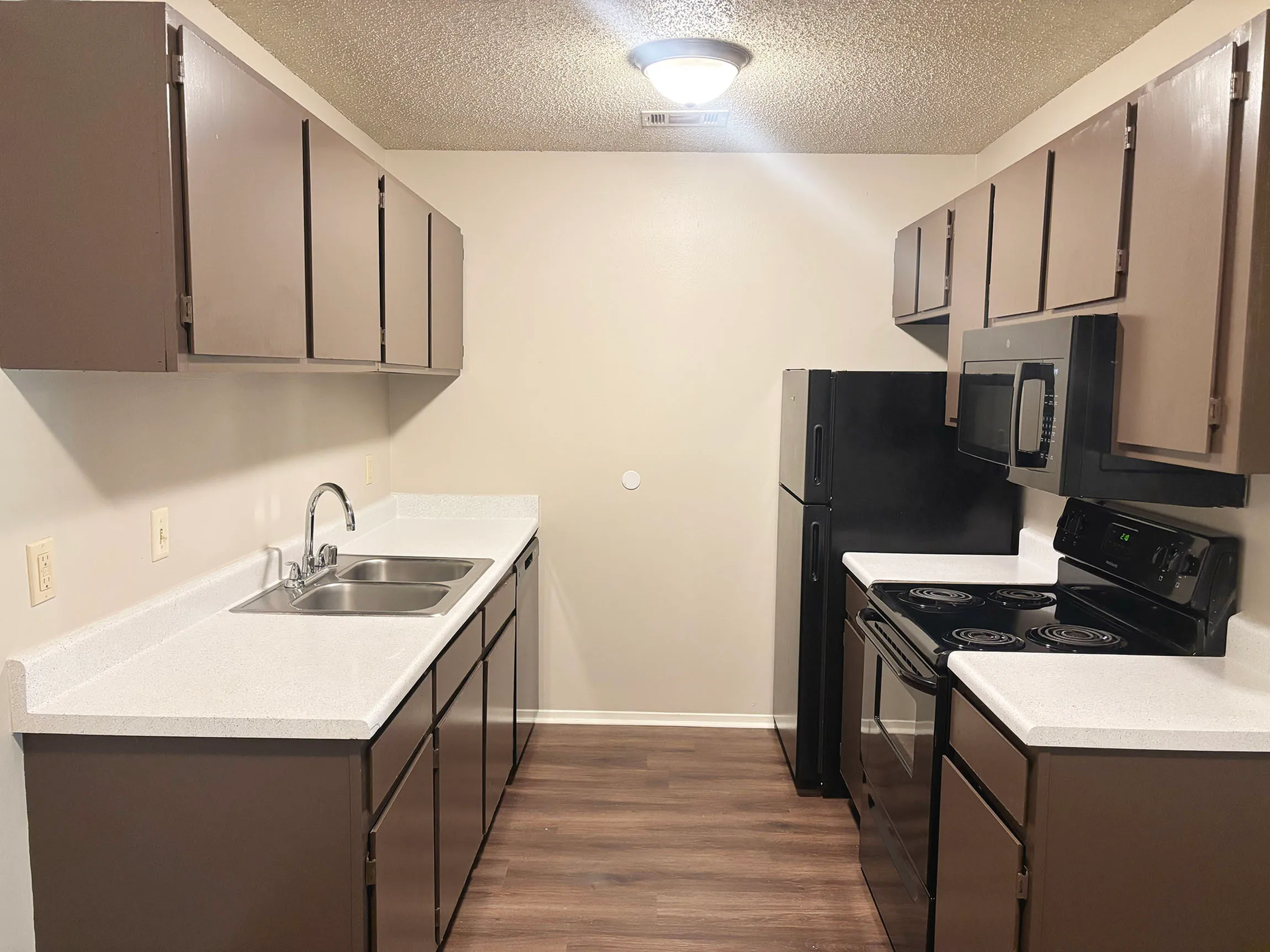 Modern galley kitchen featuring sleek dark cabinetry, white countertops, and contemporary appliances.