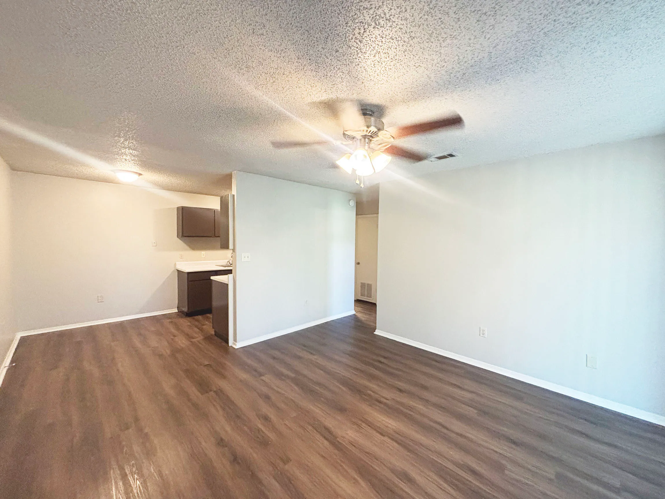 Bright and airy open-concept living space with elegant wood flooring, ceiling fan, and a modern kitchen area.