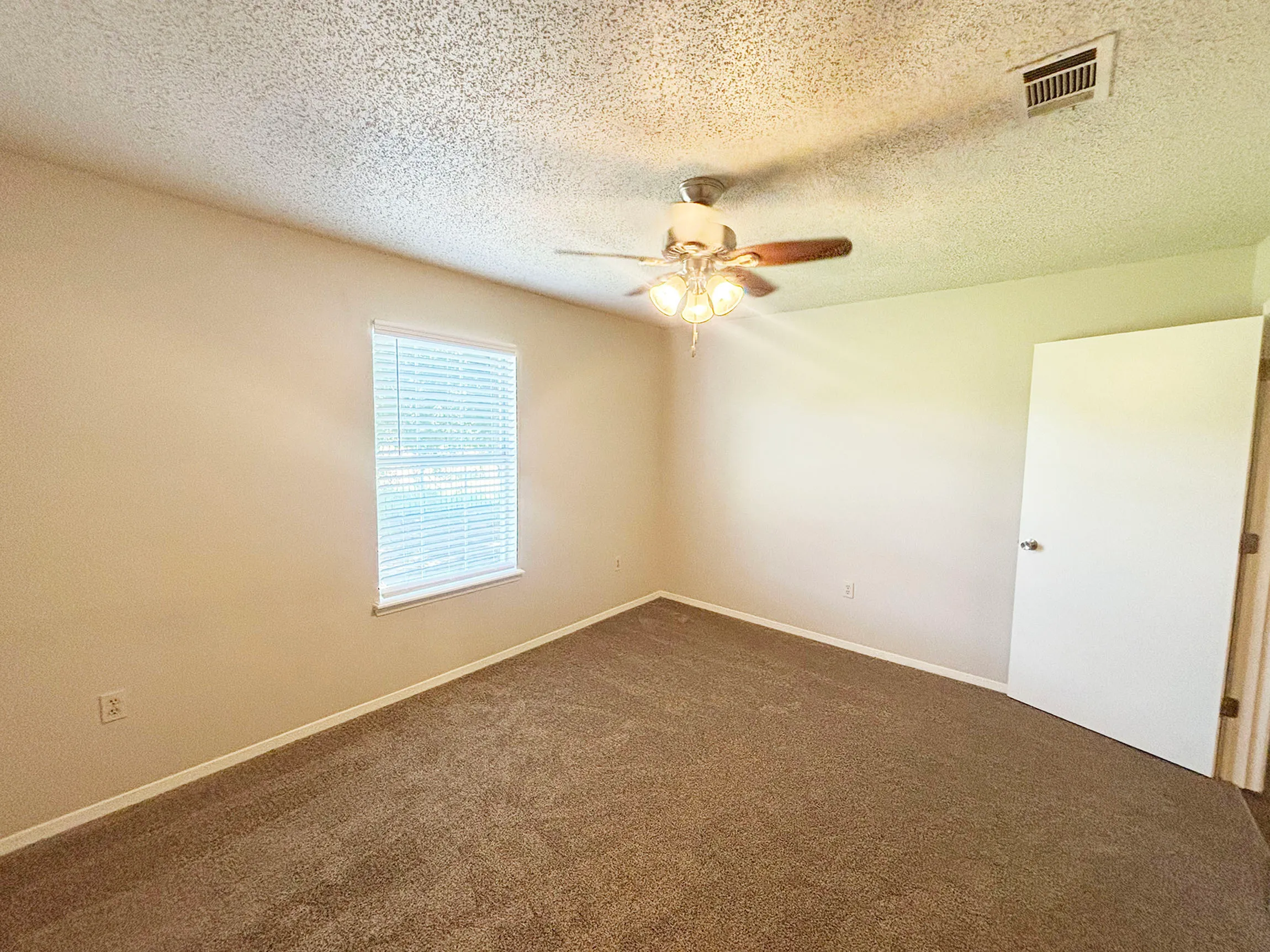 Bright, spacious bedroom with soft carpeting, modern ceiling fan, and ample natural light from a large window.