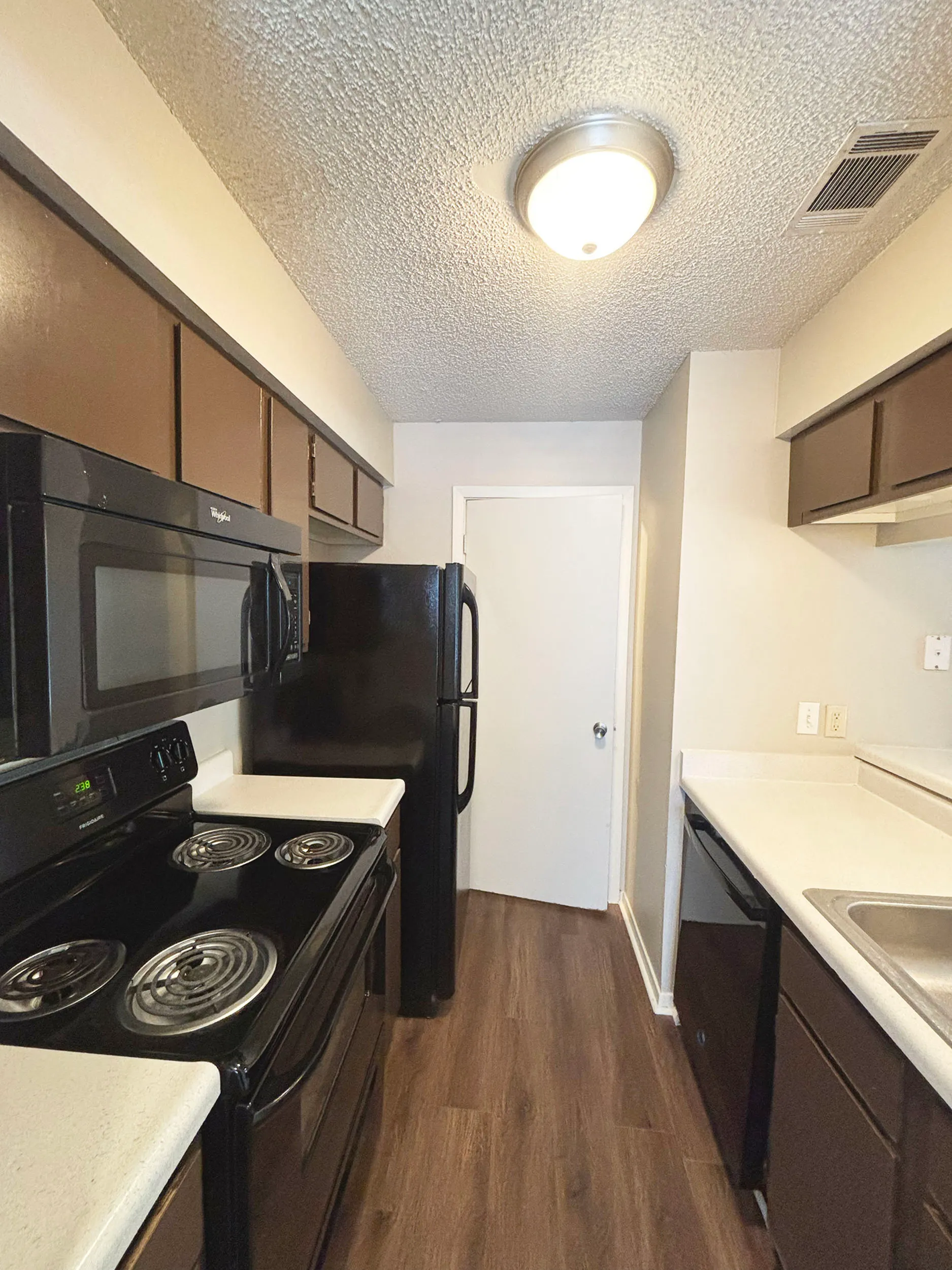 Modern kitchen with dark appliances, sleek countertops, and warm wood flooring, offering a cozy yet functional space.