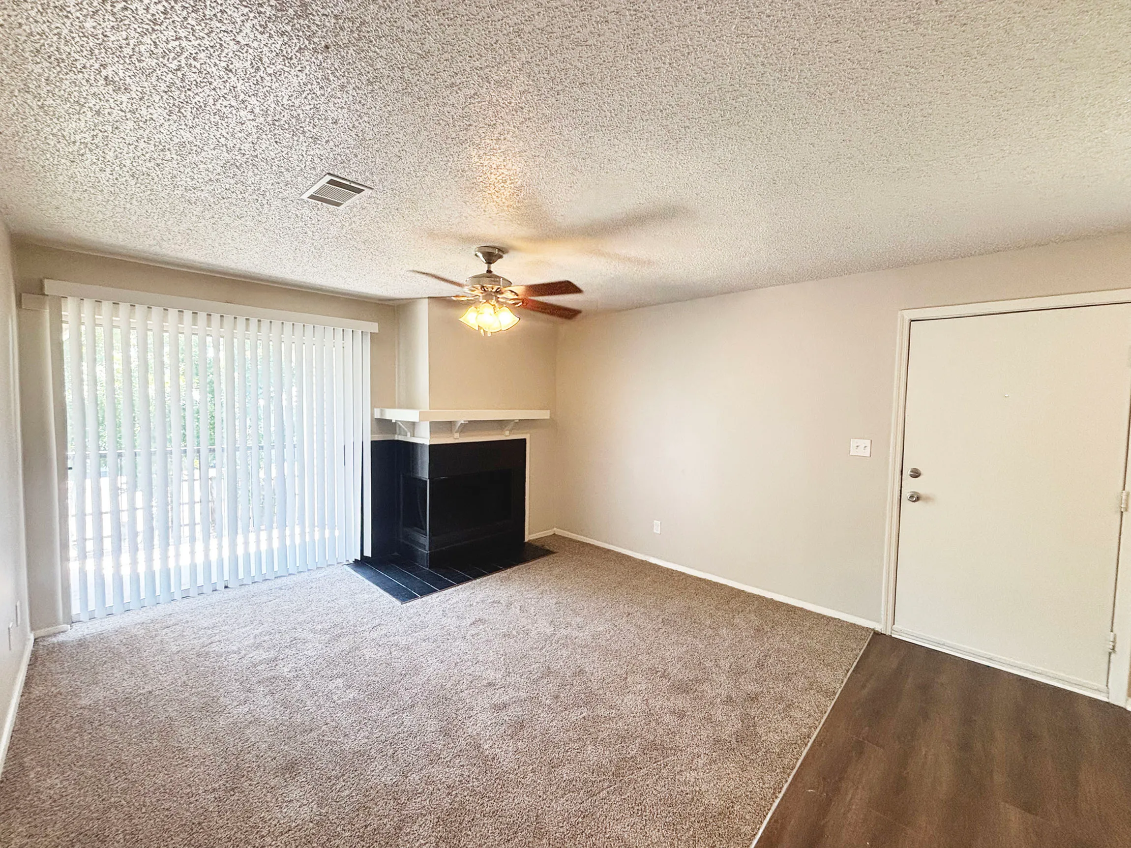 Bright living room featuring a modern ceiling fan, cozy fireplace, and ample natural light through sliding glass doors.