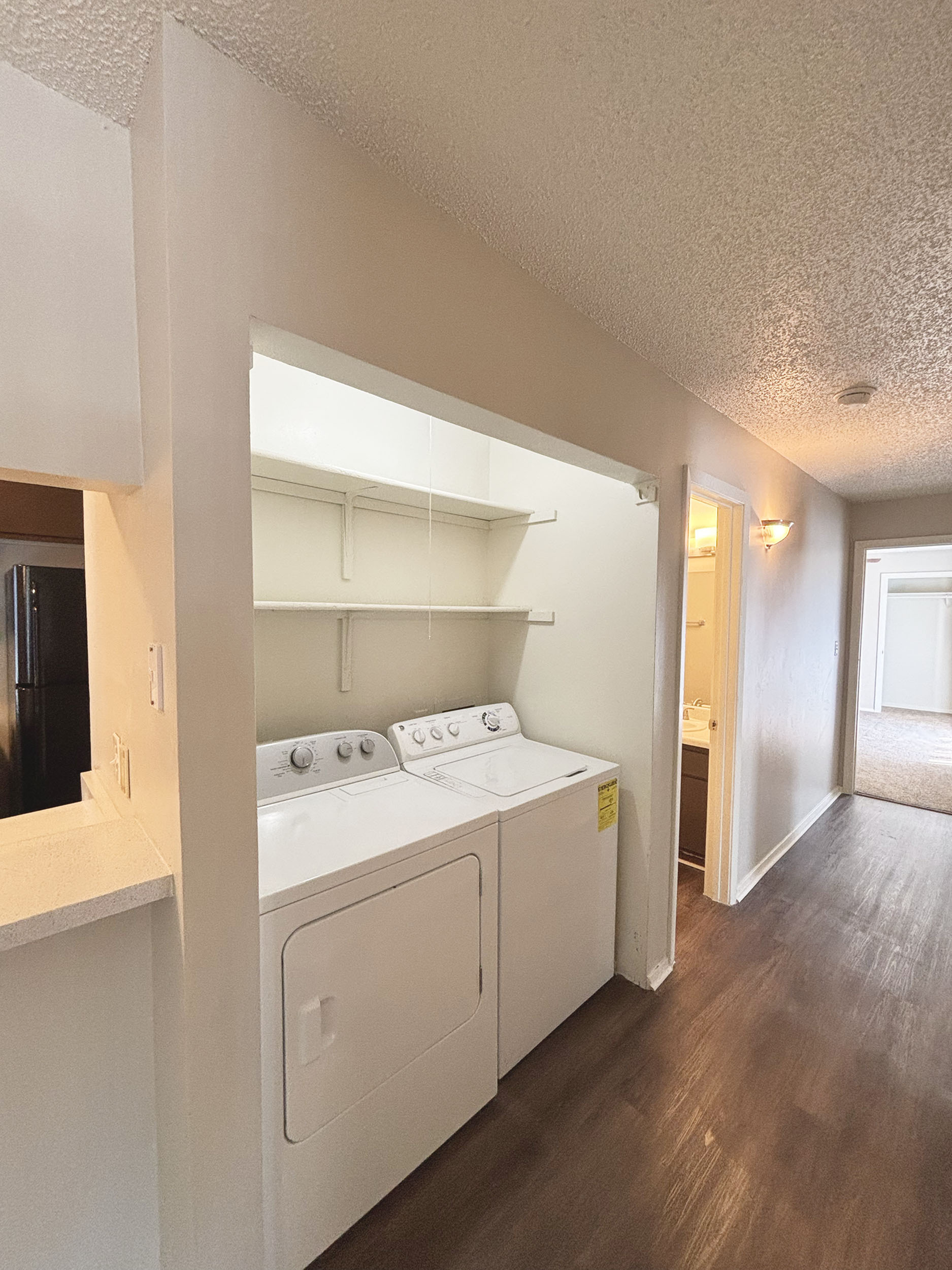 Bright apartment hallway featuring an in-unit washer and dryer, with modern lighting and sleek vinyl flooring.