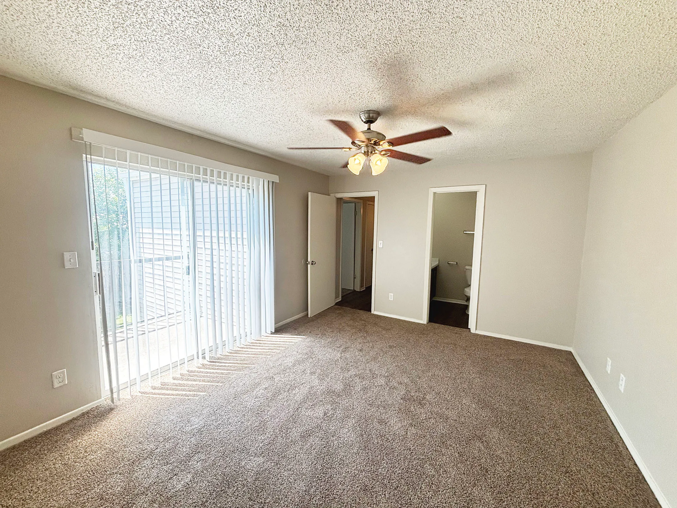 Bright and spacious bedroom with plush carpet, ceiling fan, and large window for natural light.