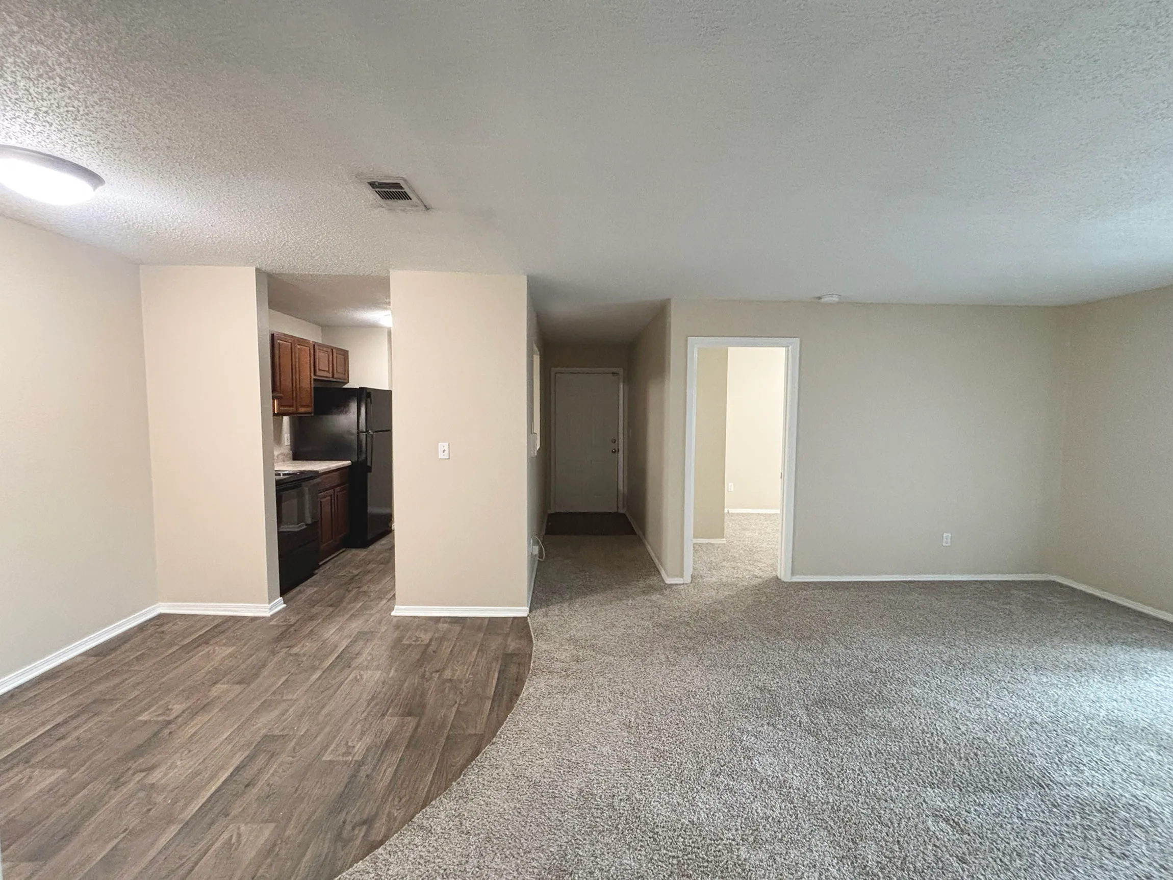 Modern apartment interior featuring an open-concept living area with plush carpet, adjacent to a sleek kitchen with wooden cabinetry and dark appliances.