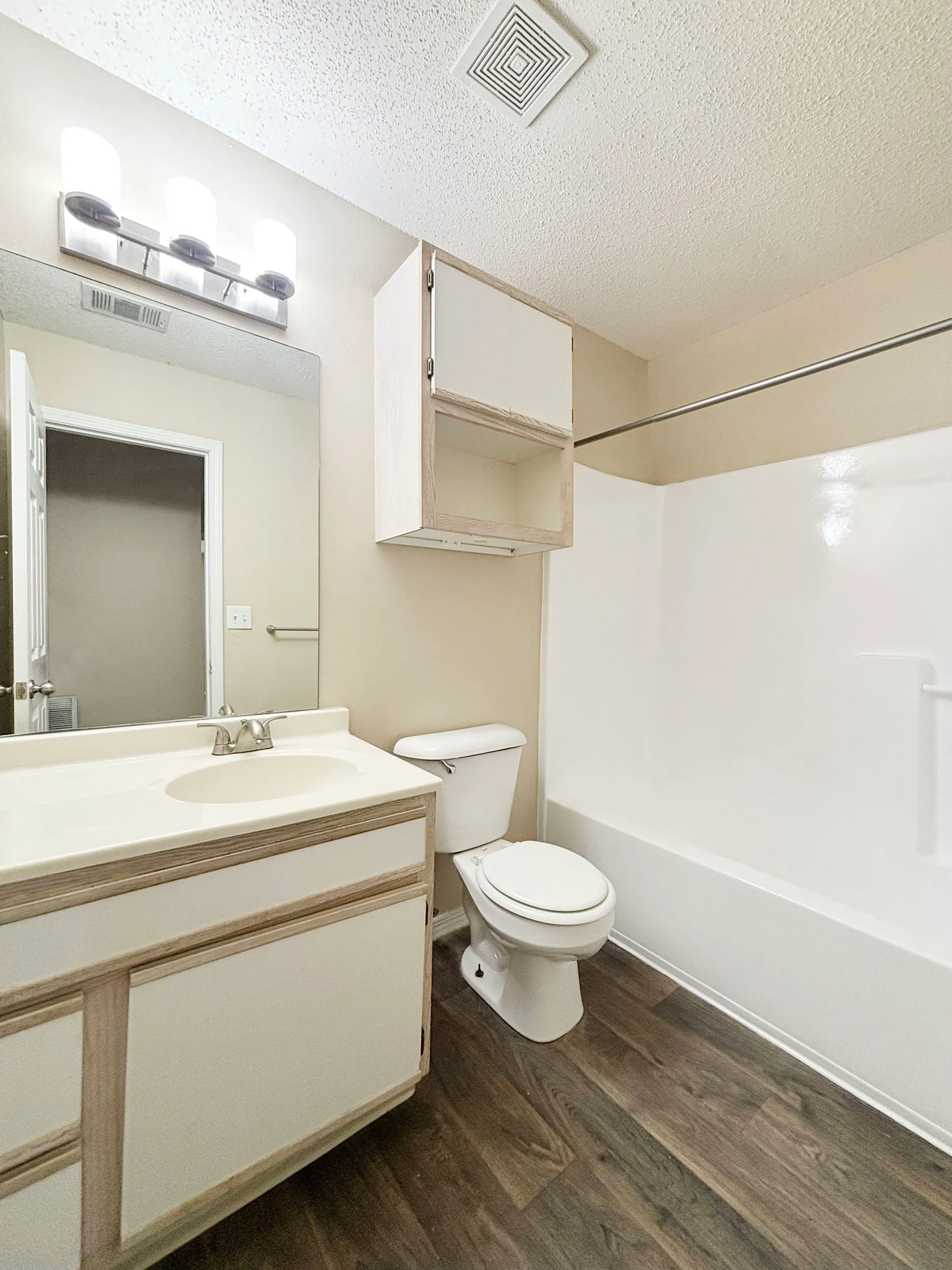 Modern bathroom featuring elegant lighting, a sleek vanity, and a spacious bathtub complemented by wood-style flooring.