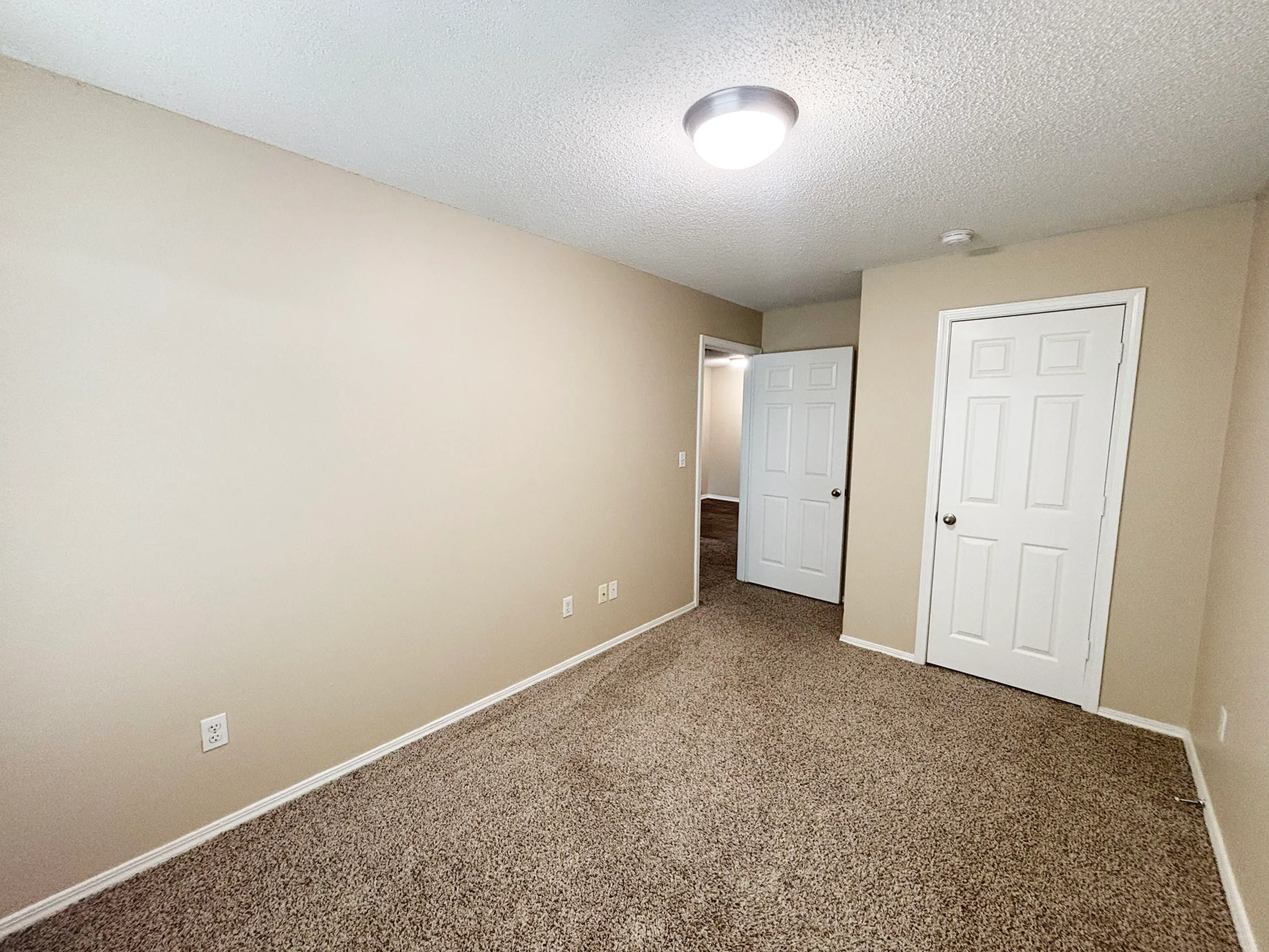 Bright and spacious room with plush carpet, neutral walls, and modern lighting, offering a blank canvas for personal touches.