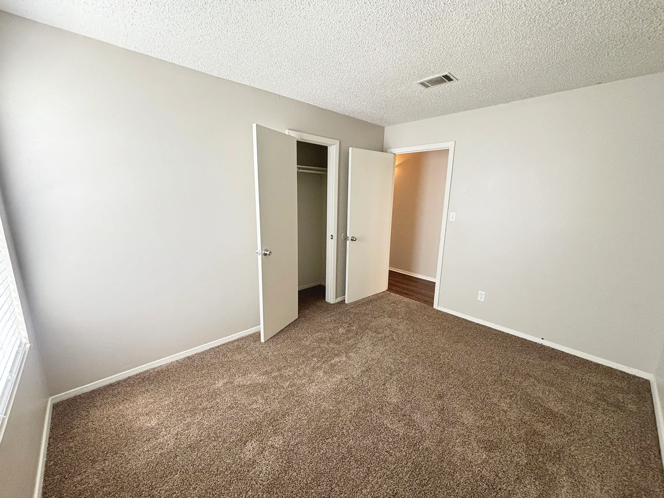 Spacious bedroom with soft carpet flooring and ample natural light, featuring an open closet and neutral color walls.