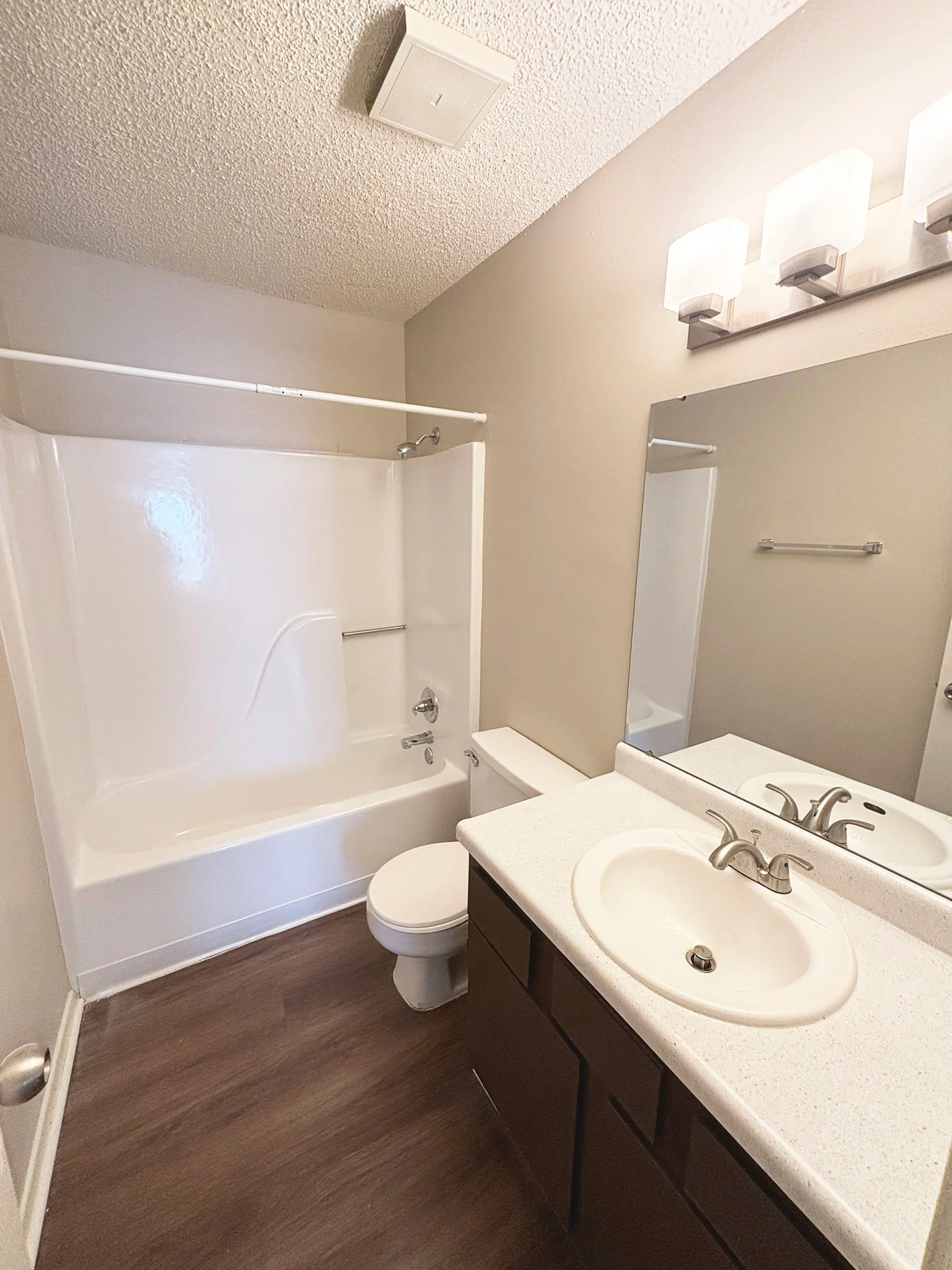 Modern bathroom with sleek white fixtures, elegant lighting, and wood-style flooring.