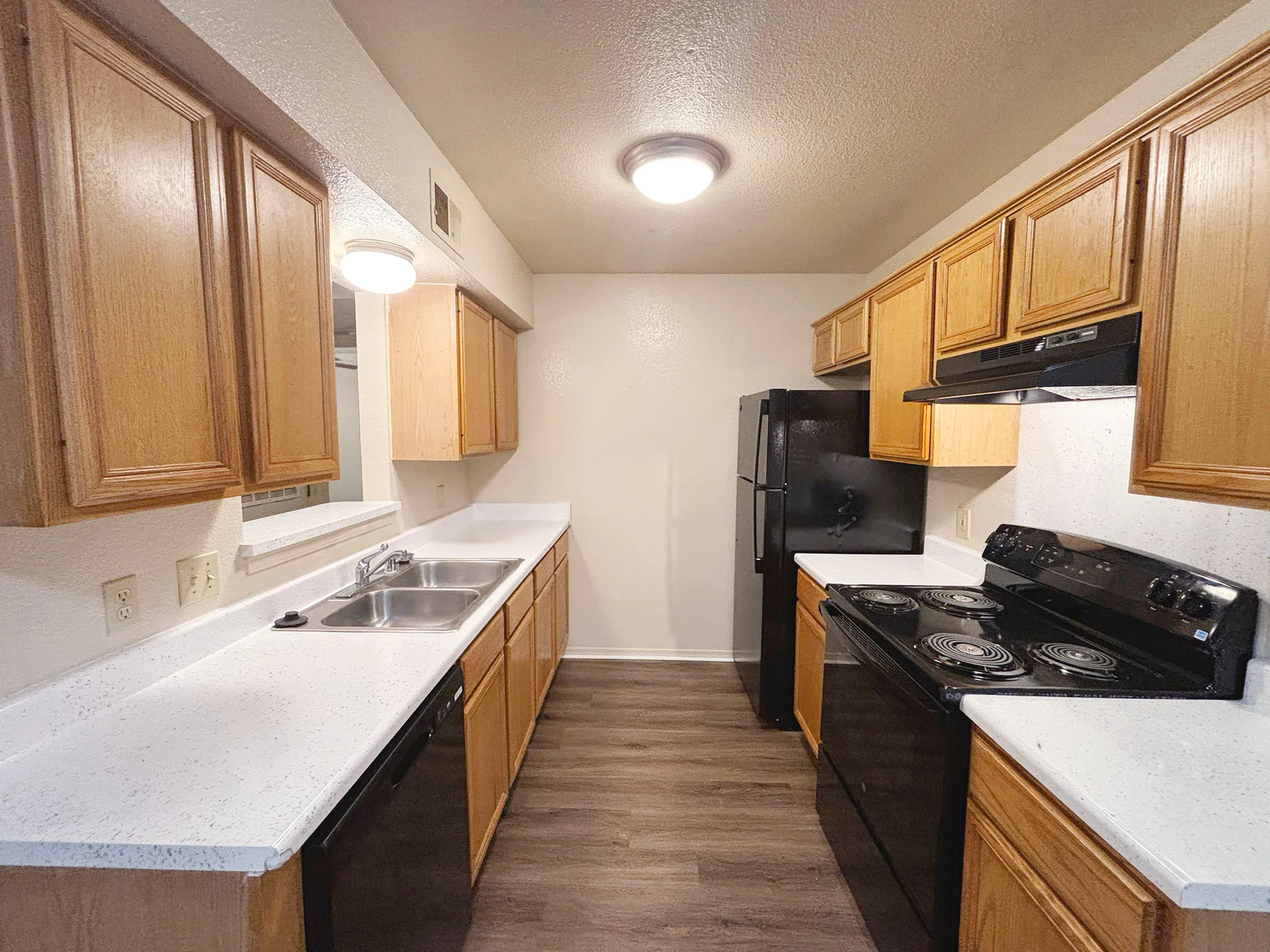 Modern kitchen boasting sleek white countertops, wooden cabinetry, and black appliances in a cozy setting.